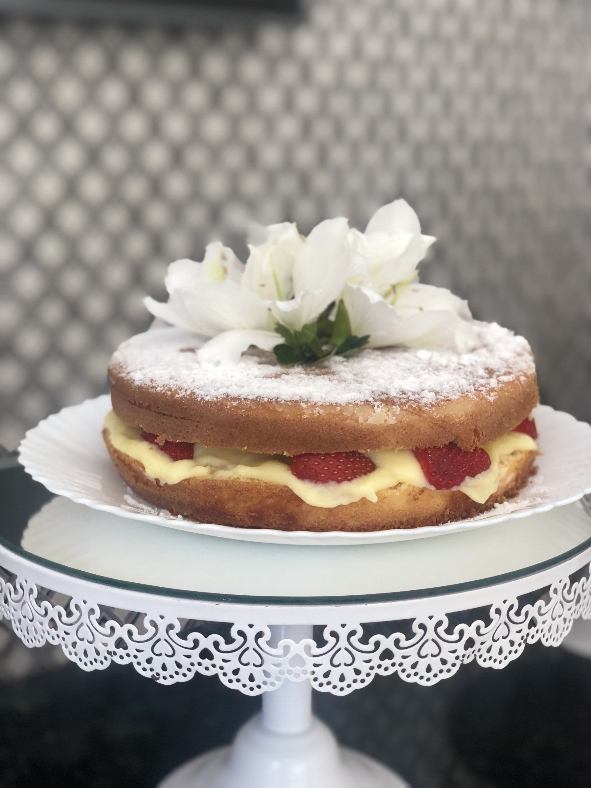 Um bolo em um prato com açúcar de confeiteiro e flores no topo