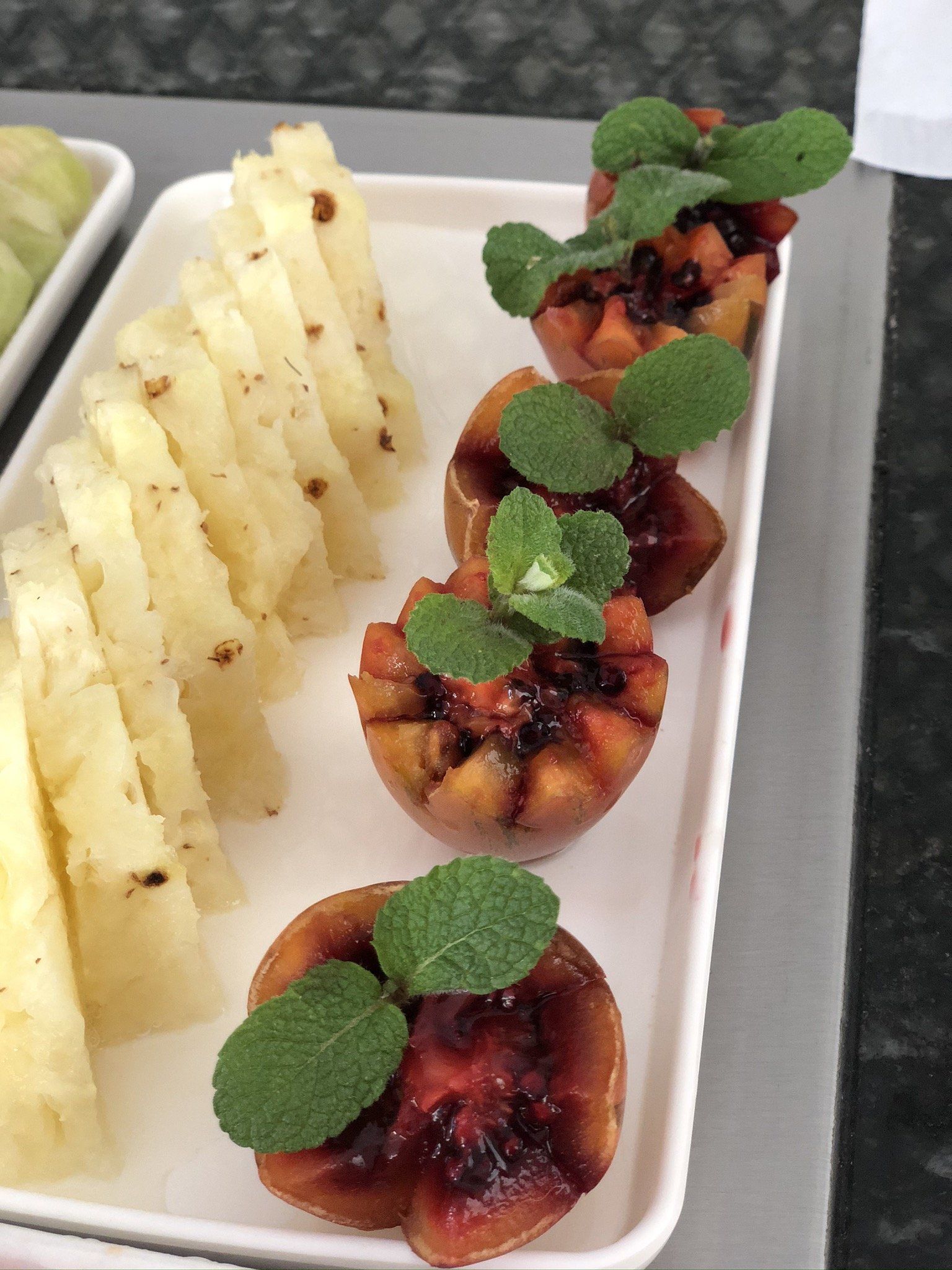 Um prato branco coberto com fatias de abacaxi e copos de frutas