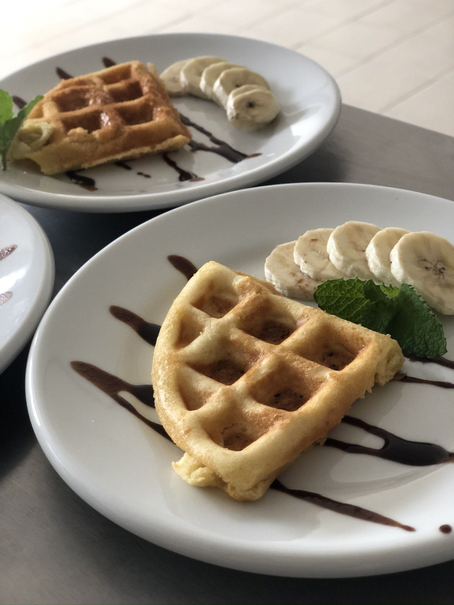 Dois pratos de waffles com bananas e calda de chocolate