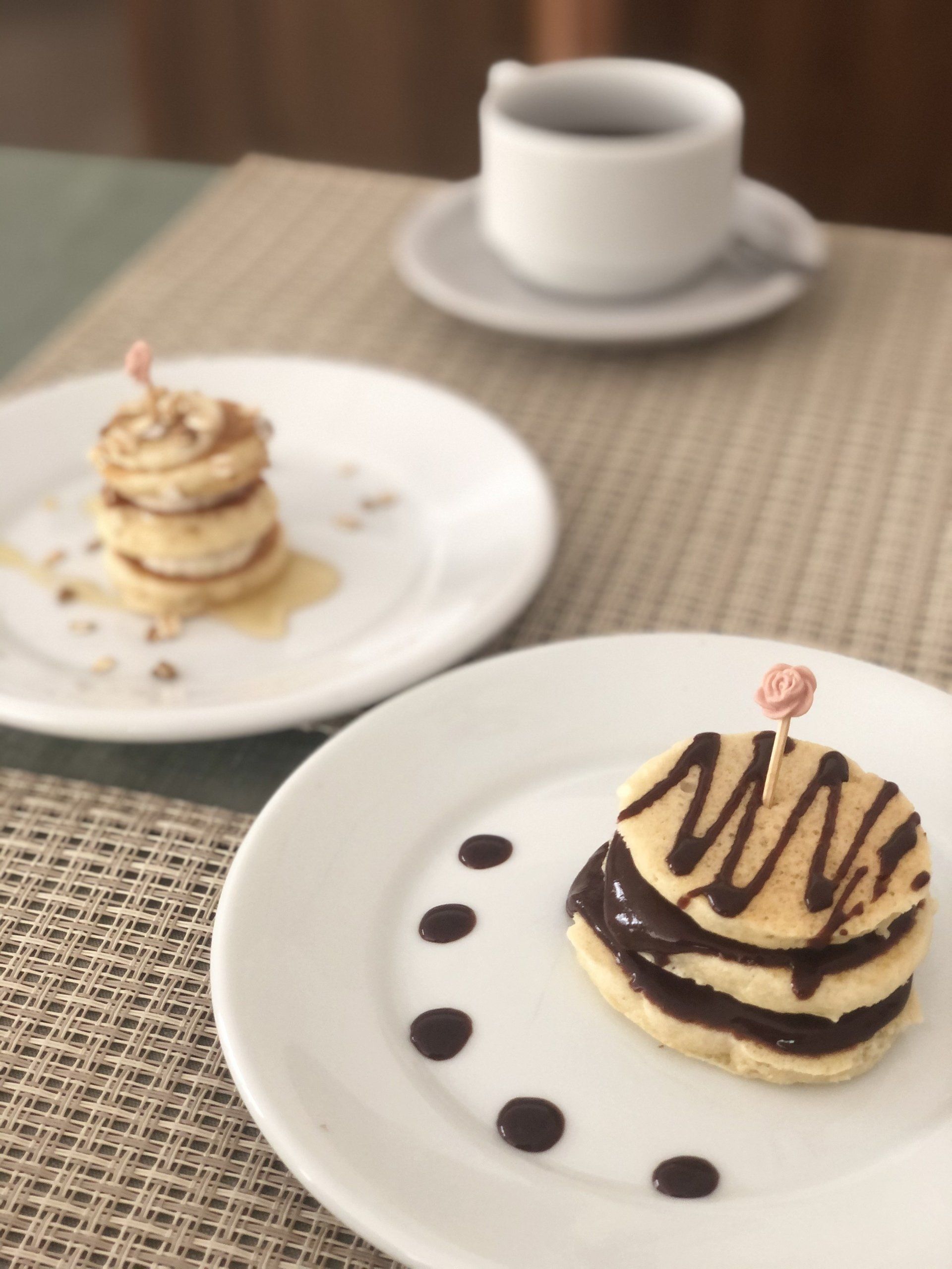 Uma pilha de panquecas em um prato ao lado de uma xícara de café