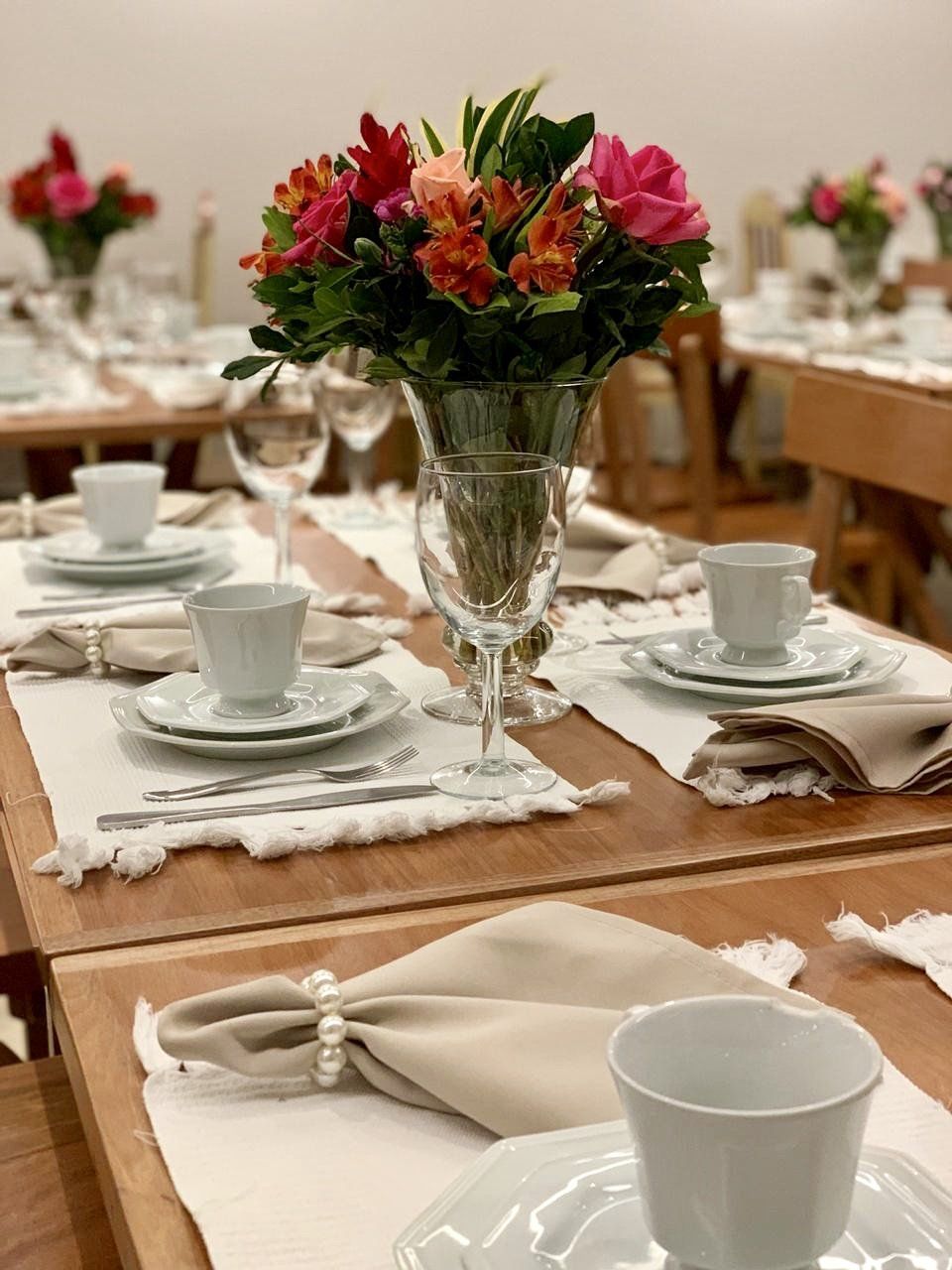 Uma mesa posta para um jantar com pratos, xícaras, copos e um vaso de flores.