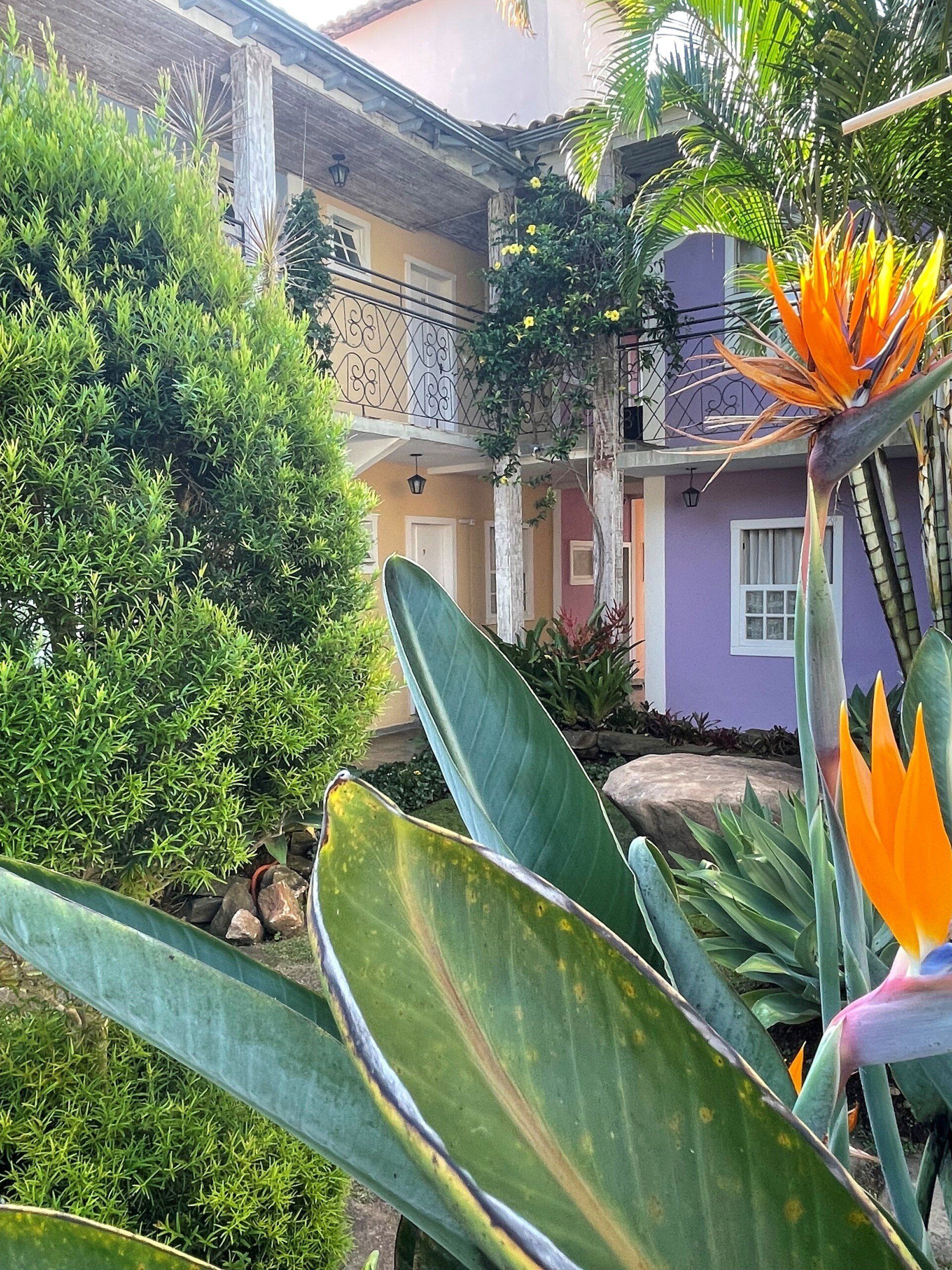 Uma casa roxa com varanda é cercada por flores e árvores.