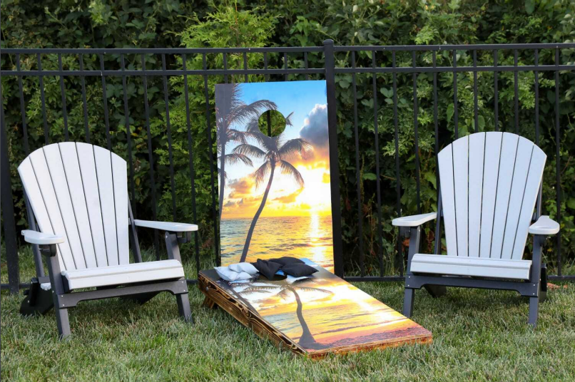 Two lawn chairs are sitting next to a cornhole board.