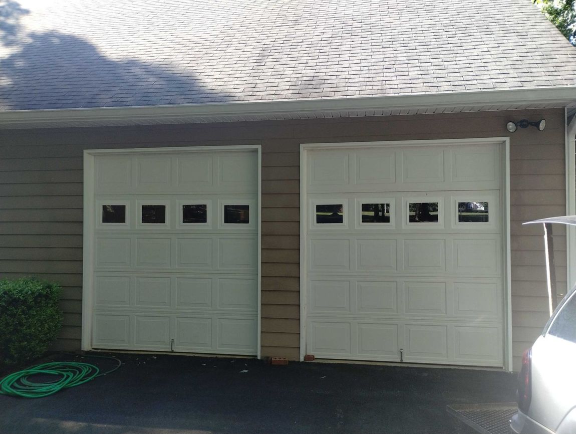 A car is parked in front of a garage with two white garage doors.