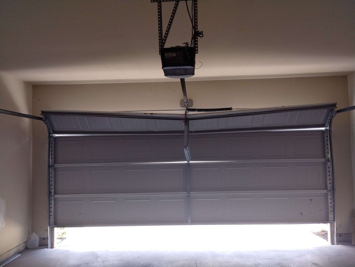 A garage door with the door open and a garage door opener hanging from the ceiling.