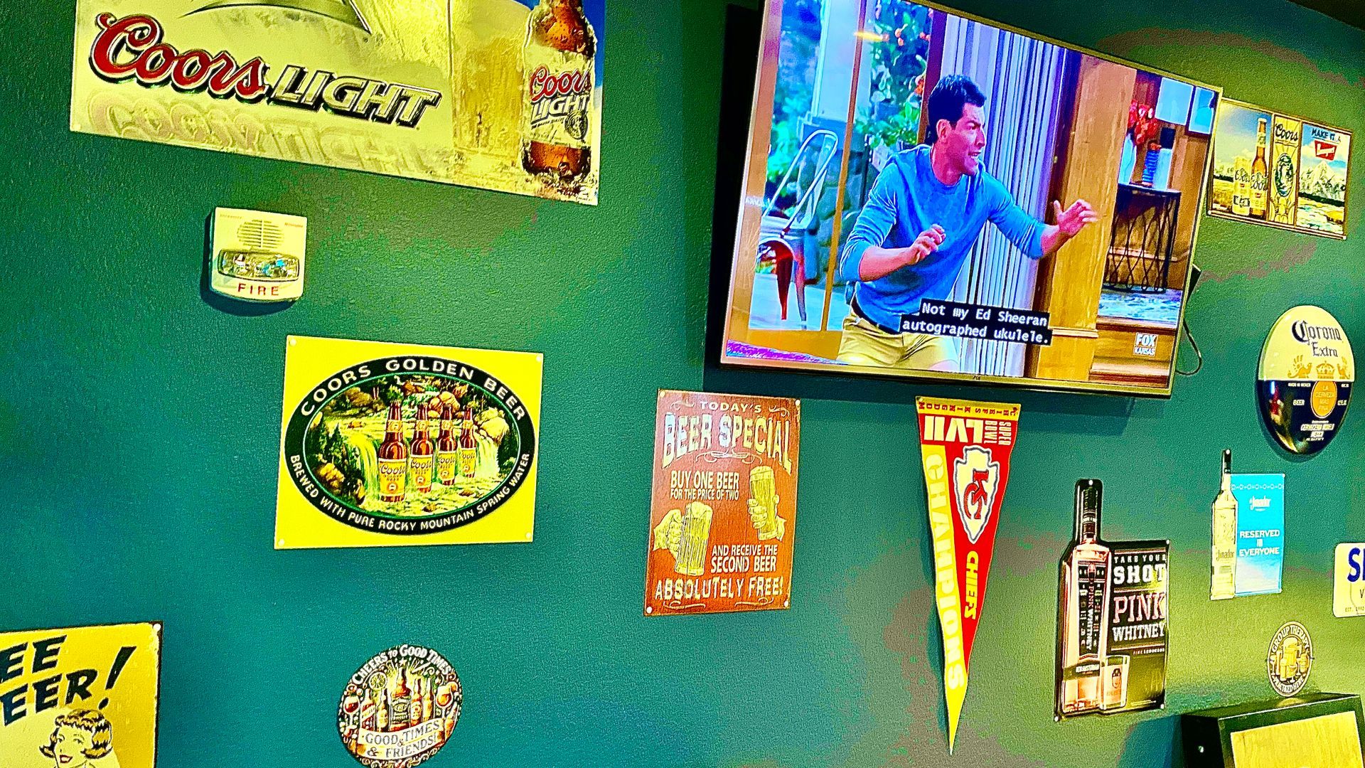 Green wall with beer signs and a TV playing a show.