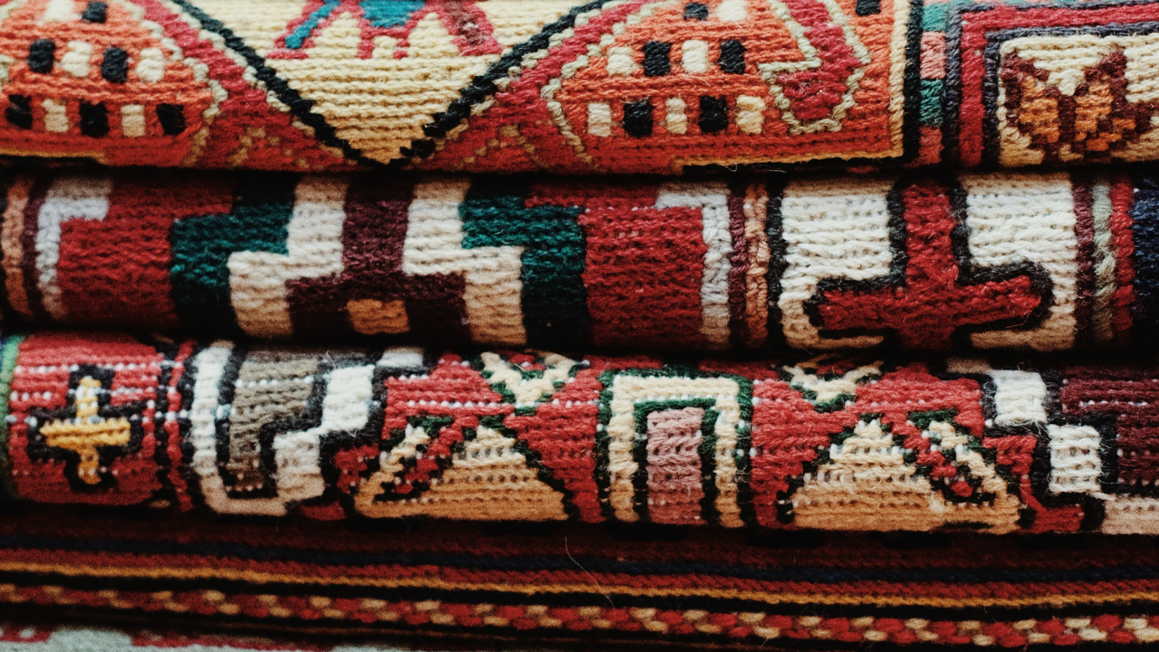 Folded patterned woven textiles in red, cream, black, and tan with geometric motifs.