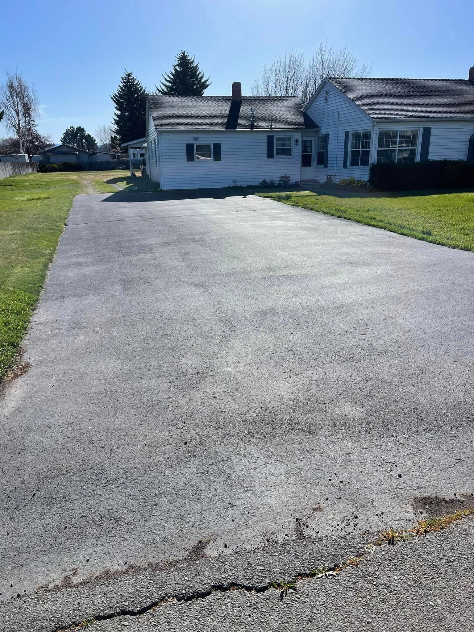 A driveway leading to a white house with a grassy yard.