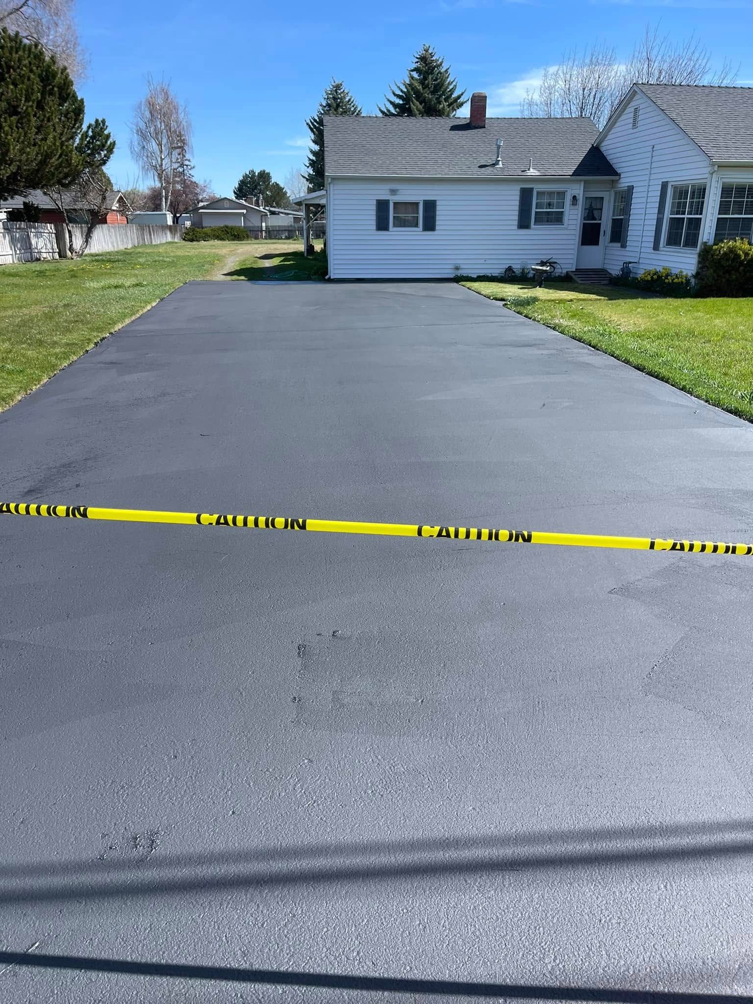 A driveway with a yellow tape along the side of it and a house in the background.