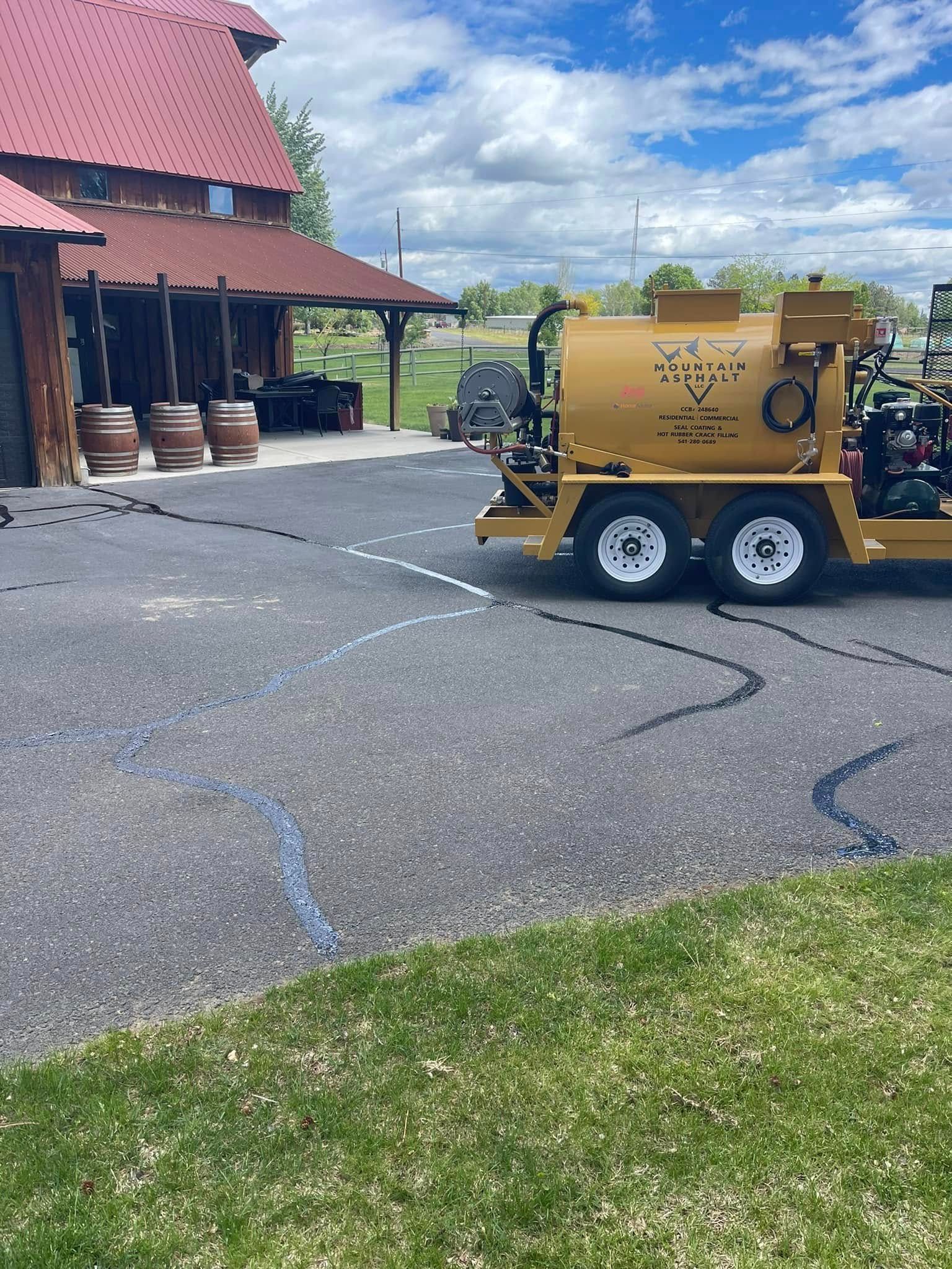 A yellow truck is parked in a parking lot in front of a barn.