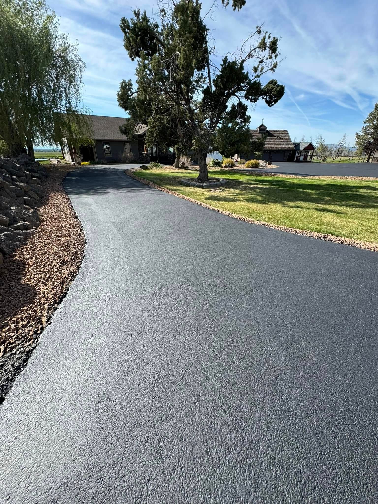 A driveway with a house in the background and trees on the side.