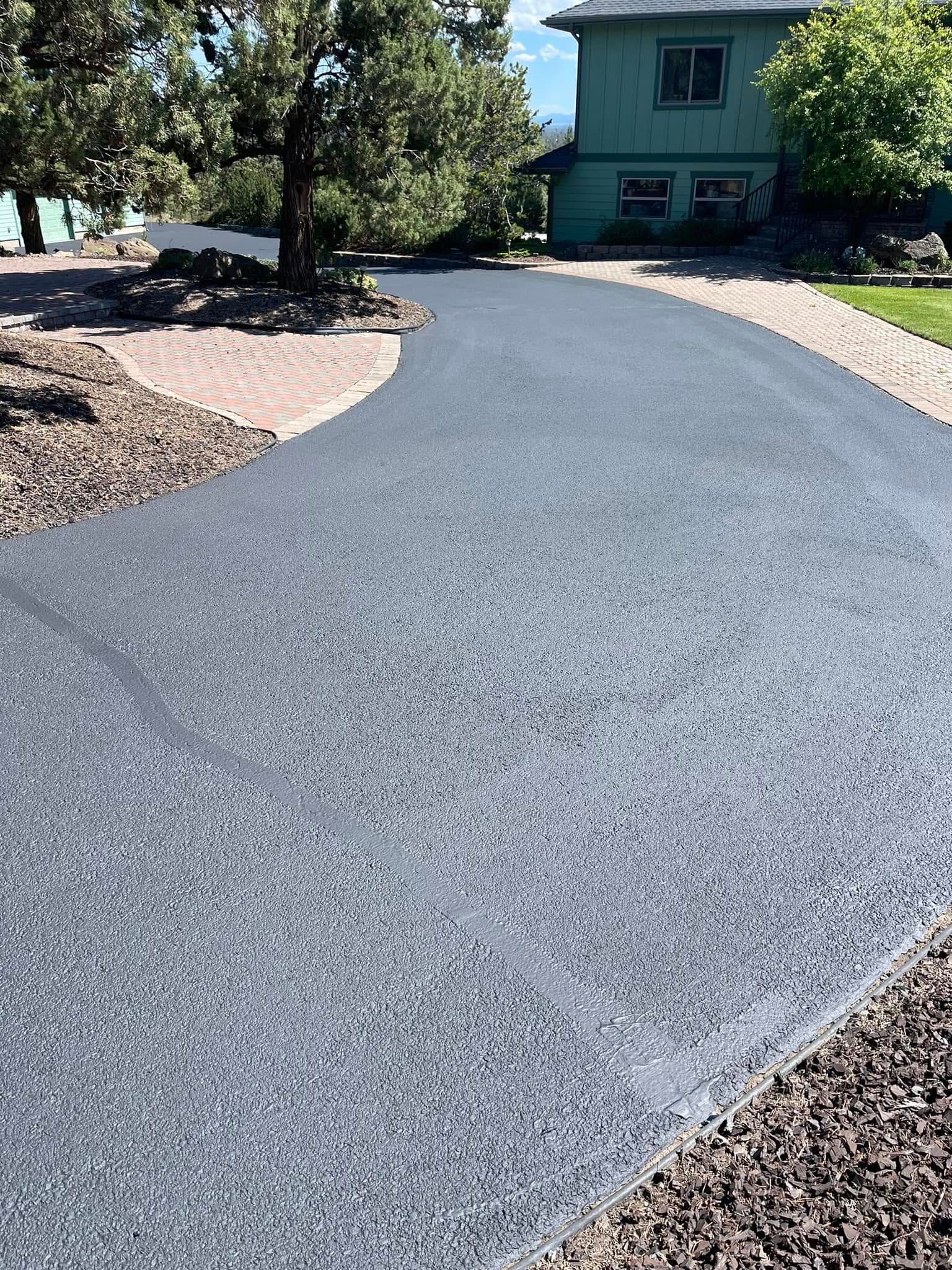 A driveway leading to a house with a green house in the background.