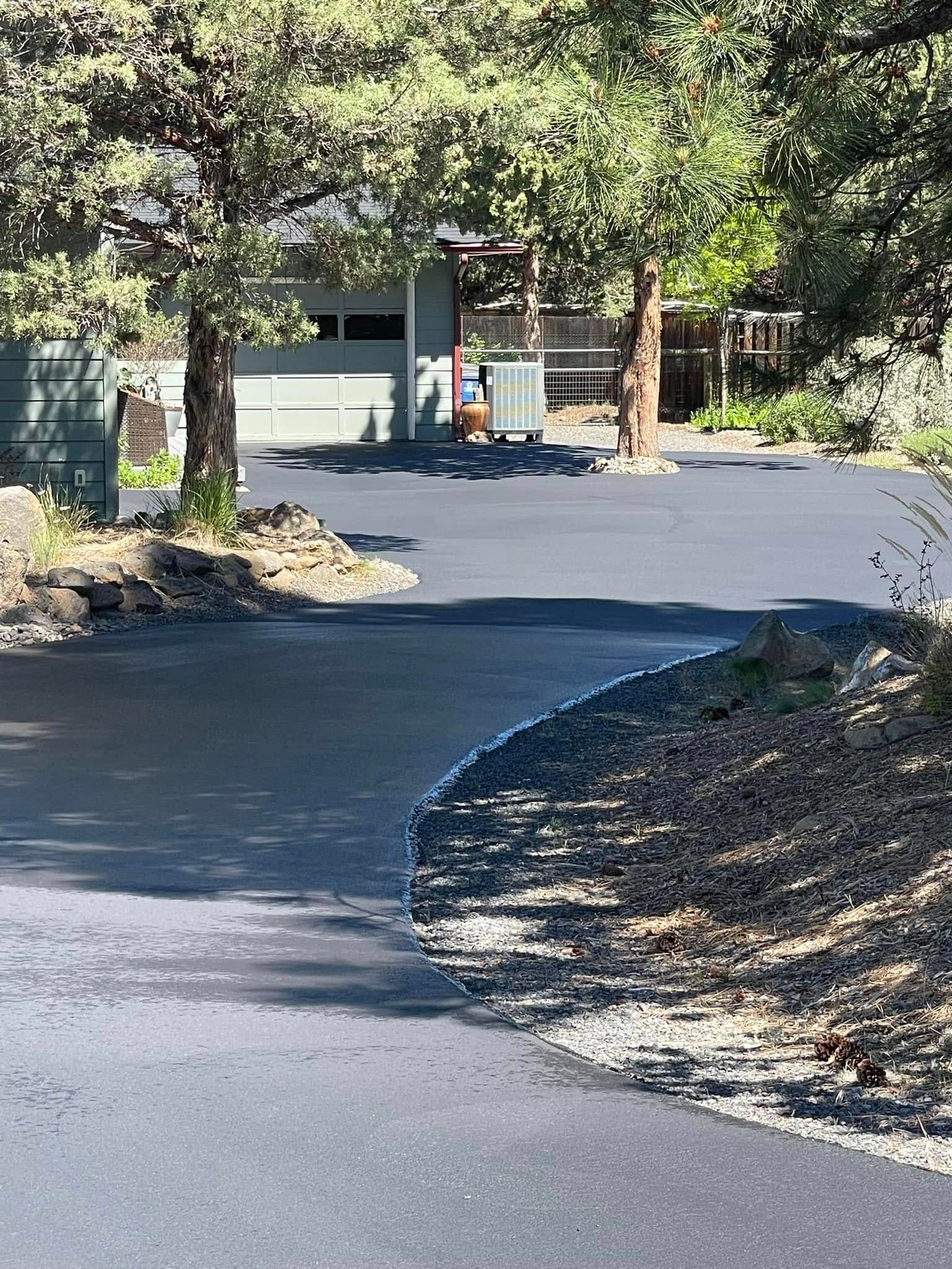A driveway with a house in the background and trees on the side of it.