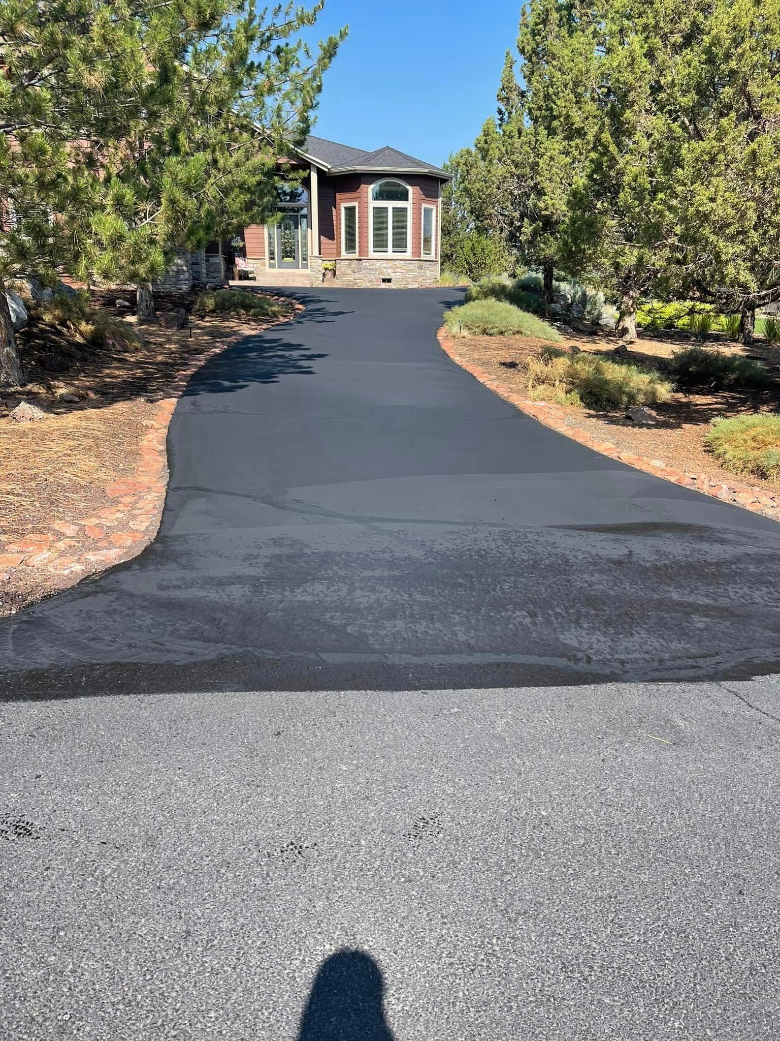 A newly paved driveway leading to a house surrounded by trees.