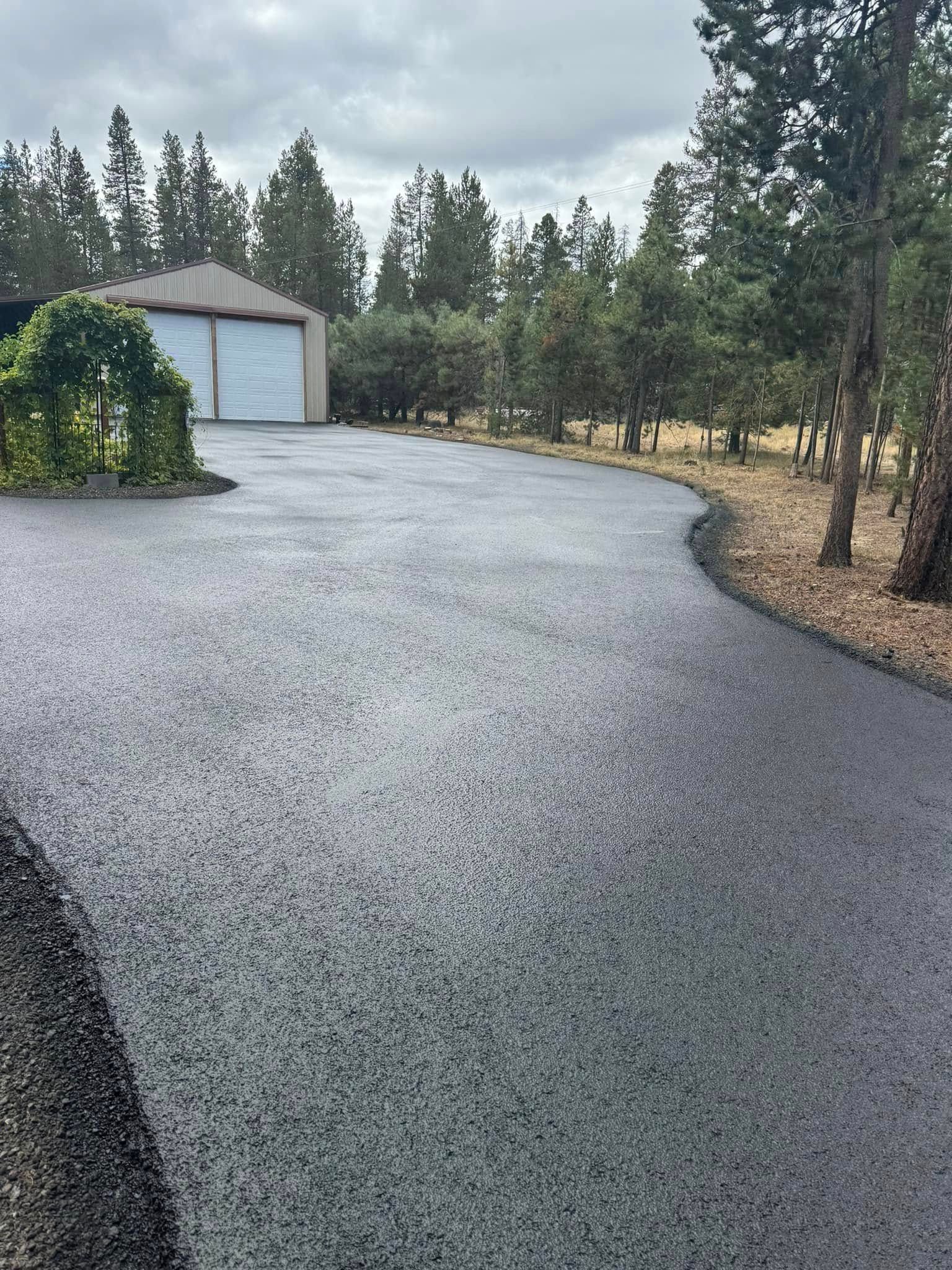 A driveway with a garage in the background and trees on the side.