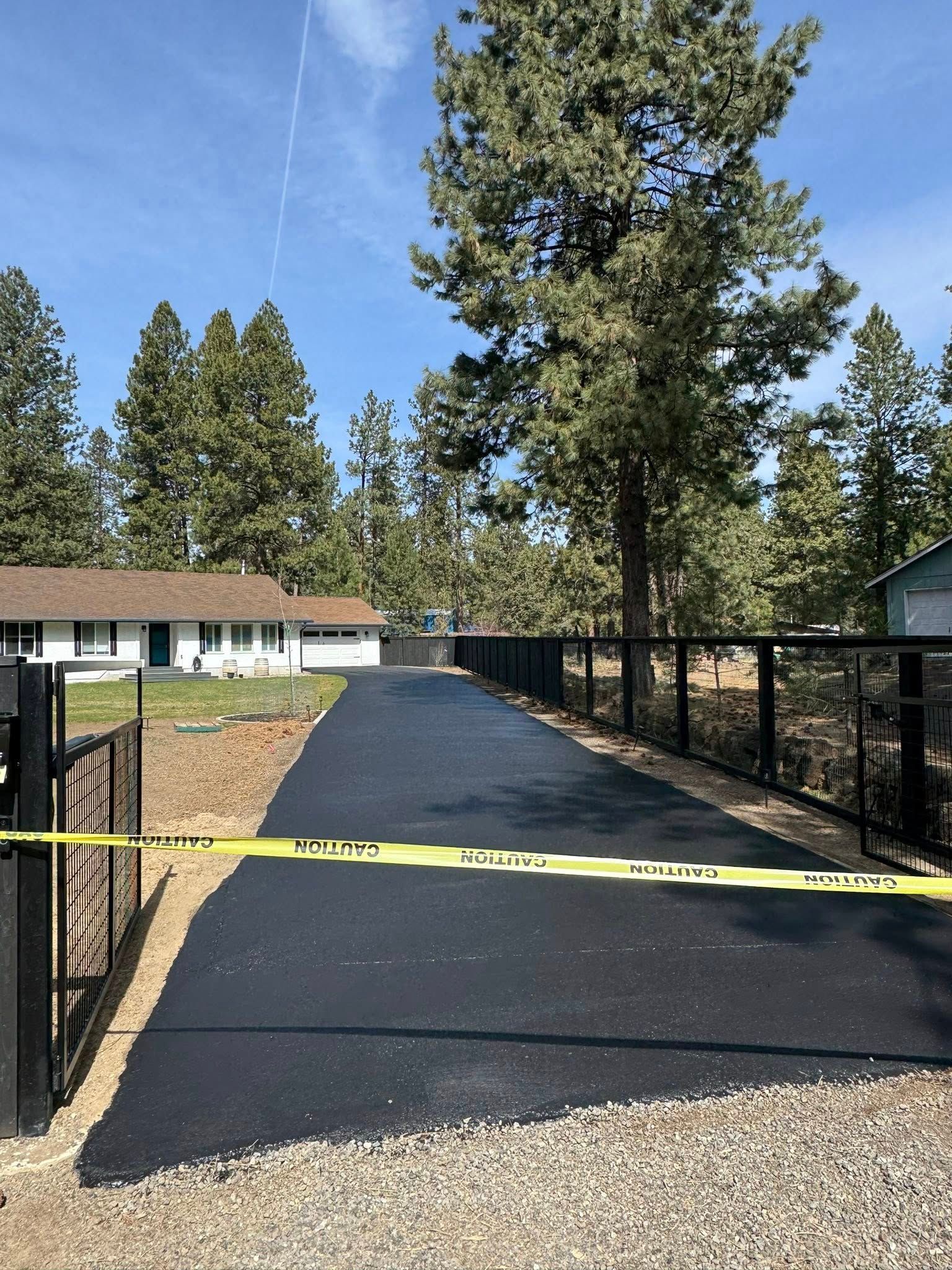 A driveway leading to a house surrounded by trees and a fence.