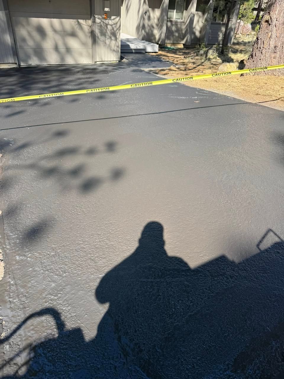 A shadow of a person is cast on the asphalt of a driveway.