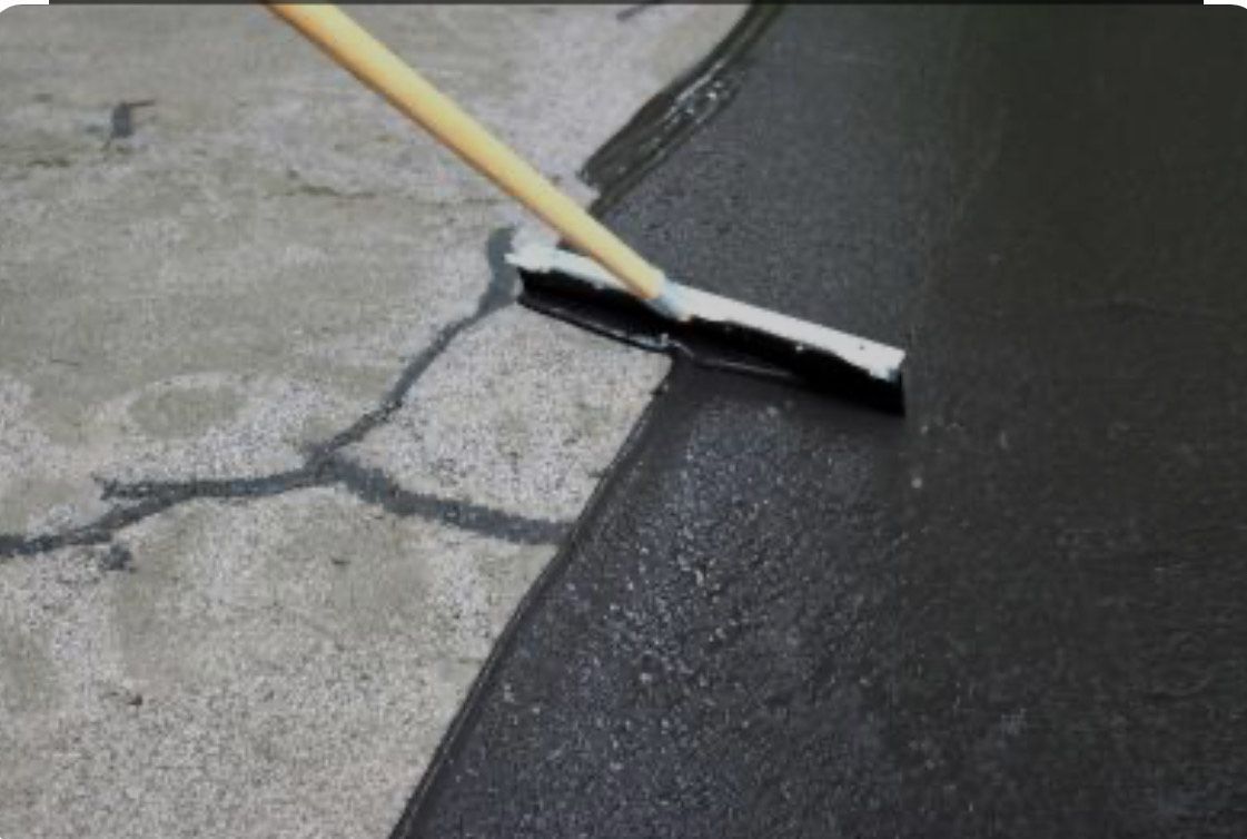 A person is using a broom to spread asphalt on the ground