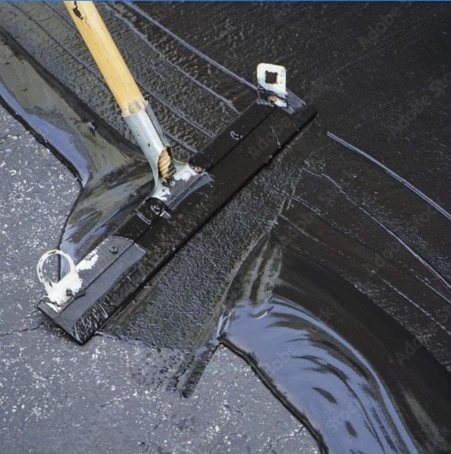 A broom is being used to spread black liquid on a concrete surface