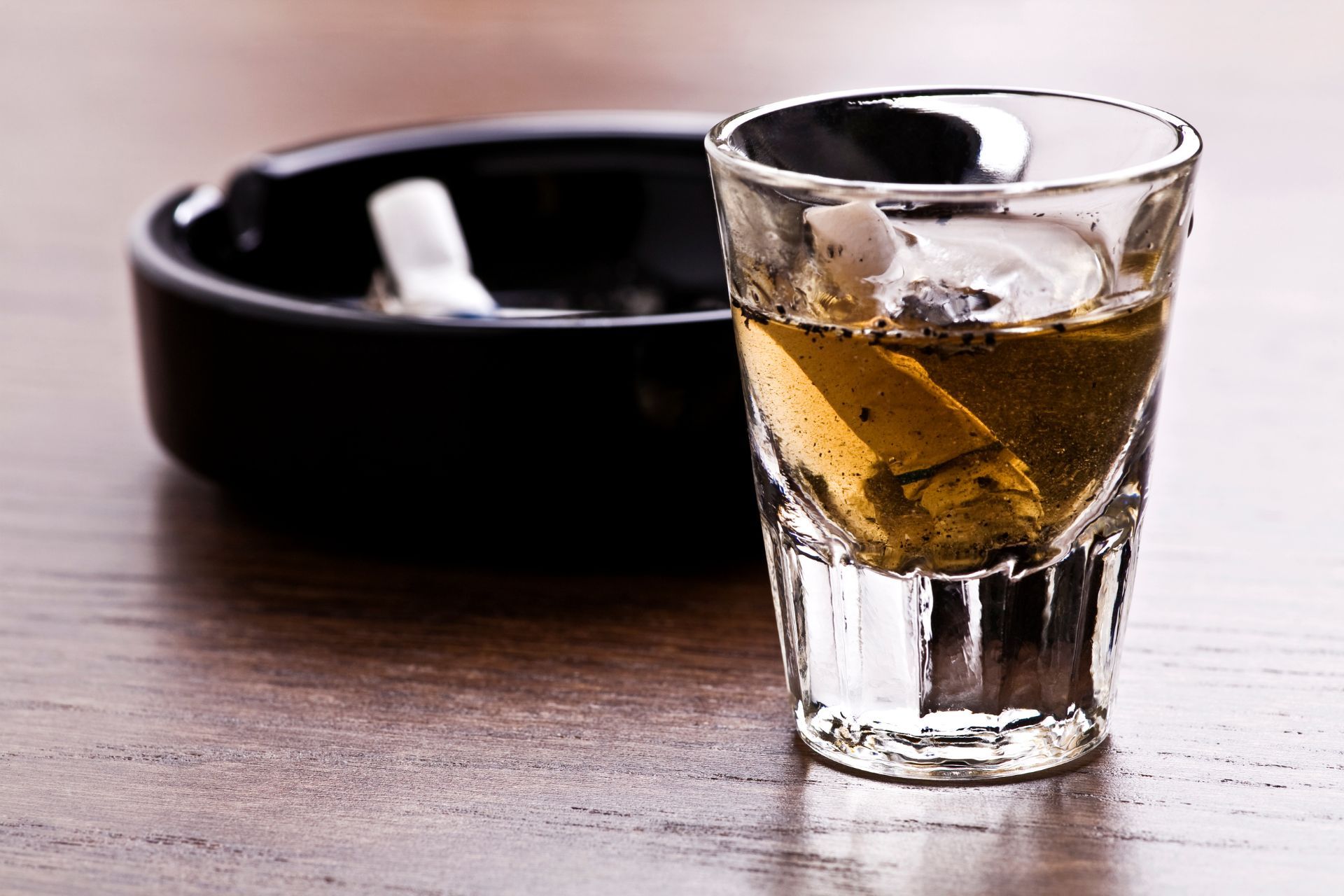 an ashtray with a cigarette butt and a shot glass with liqour on a table