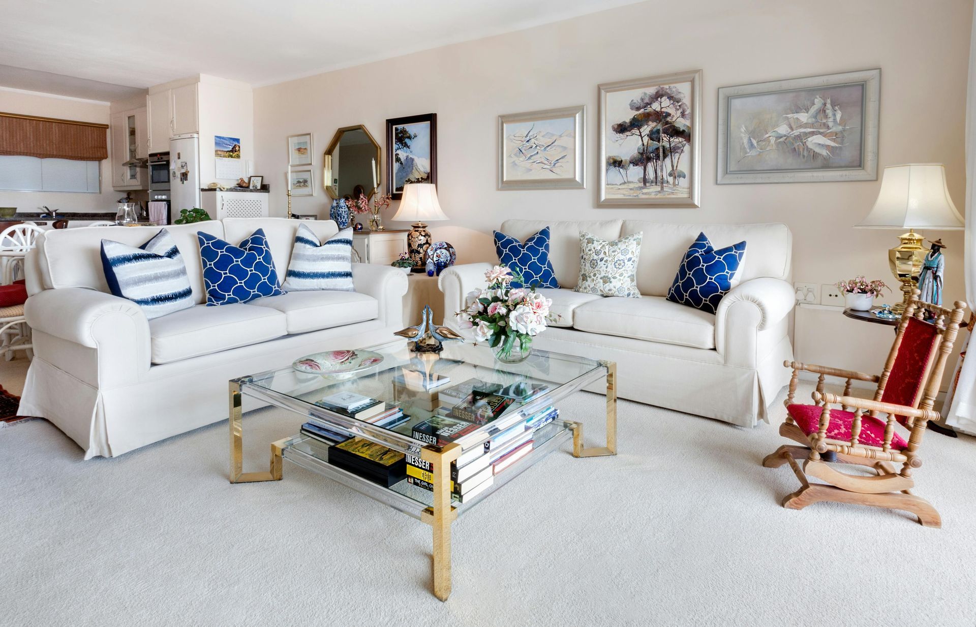 Living room with white sofas, blue pillows, and glass coffee table.