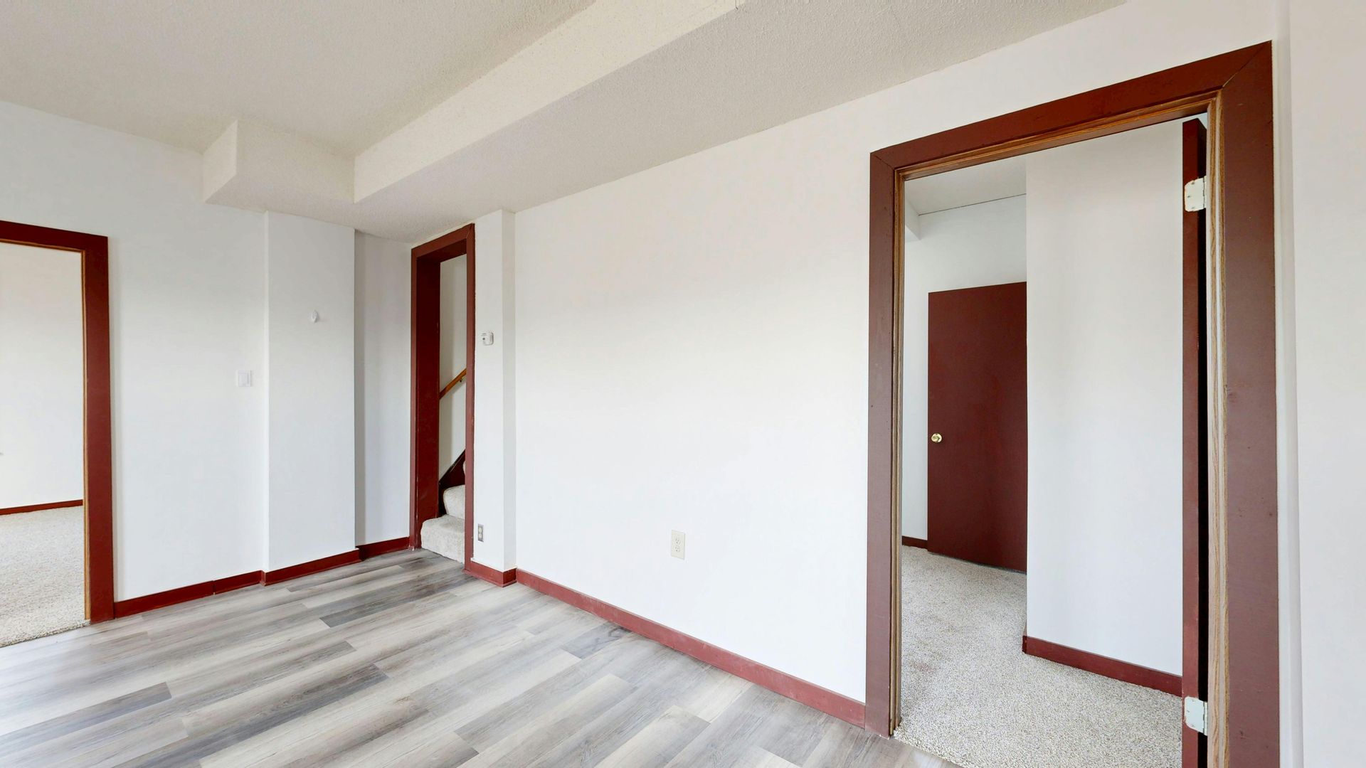 Empty room with white walls, wood trim and light wood flooring. Three doorways visible.
