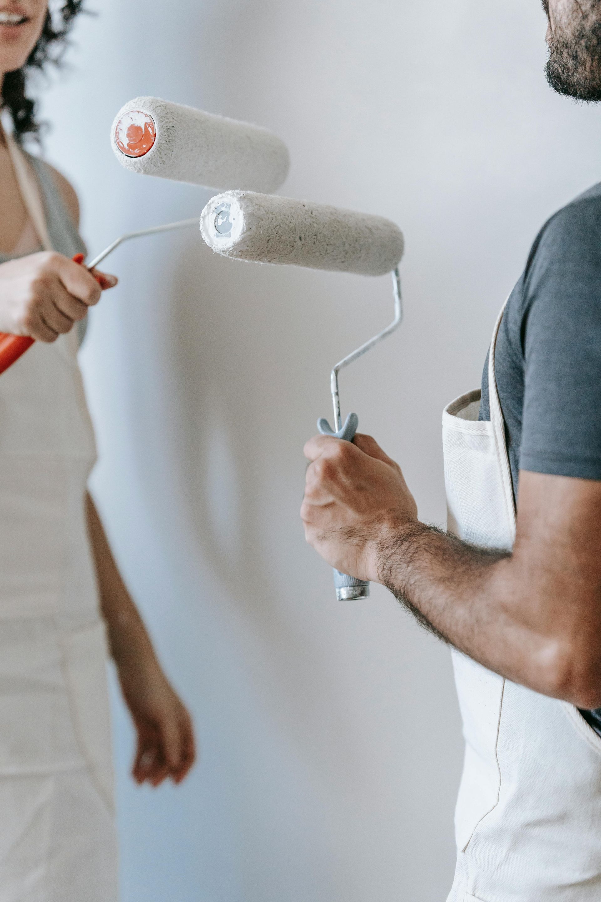 Two people holding paint rollers in front of a white wall, preparing to paint.