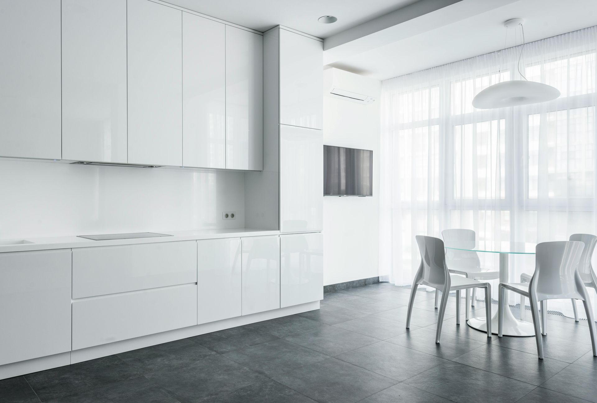 White modern kitchen with glossy cabinets, dining table, and dark gray floor.