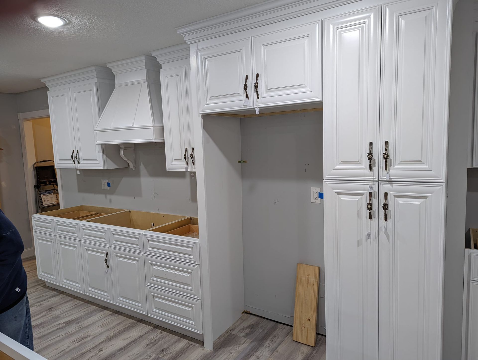 White kitchen cabinets being installed in a room with light gray walls and wood floors.