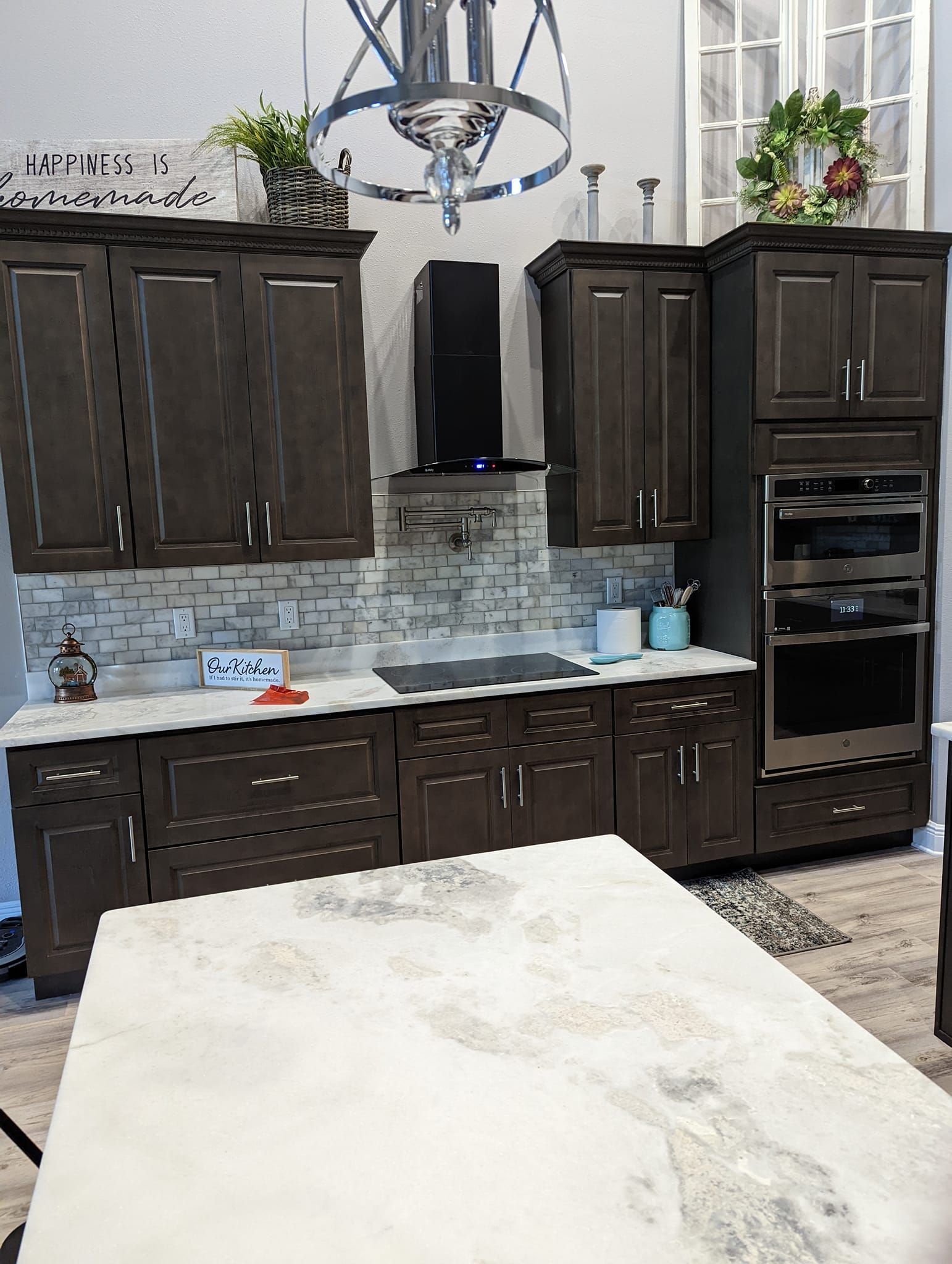 Dark wood kitchen with white countertop island, stone backsplash, and stainless steel appliances.