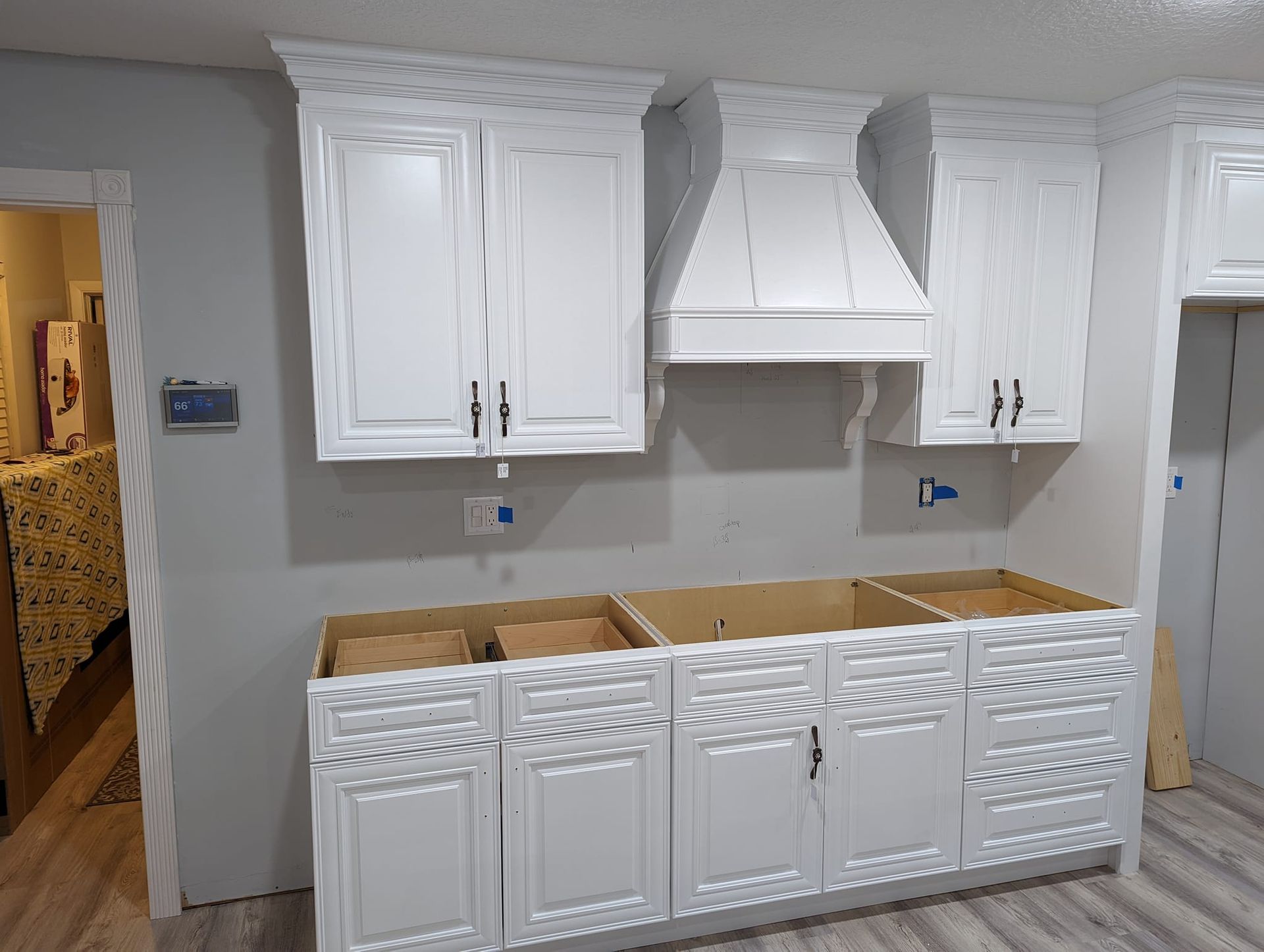 White kitchen cabinets and range hood installed on a gray wall, lower cabinets are empty.