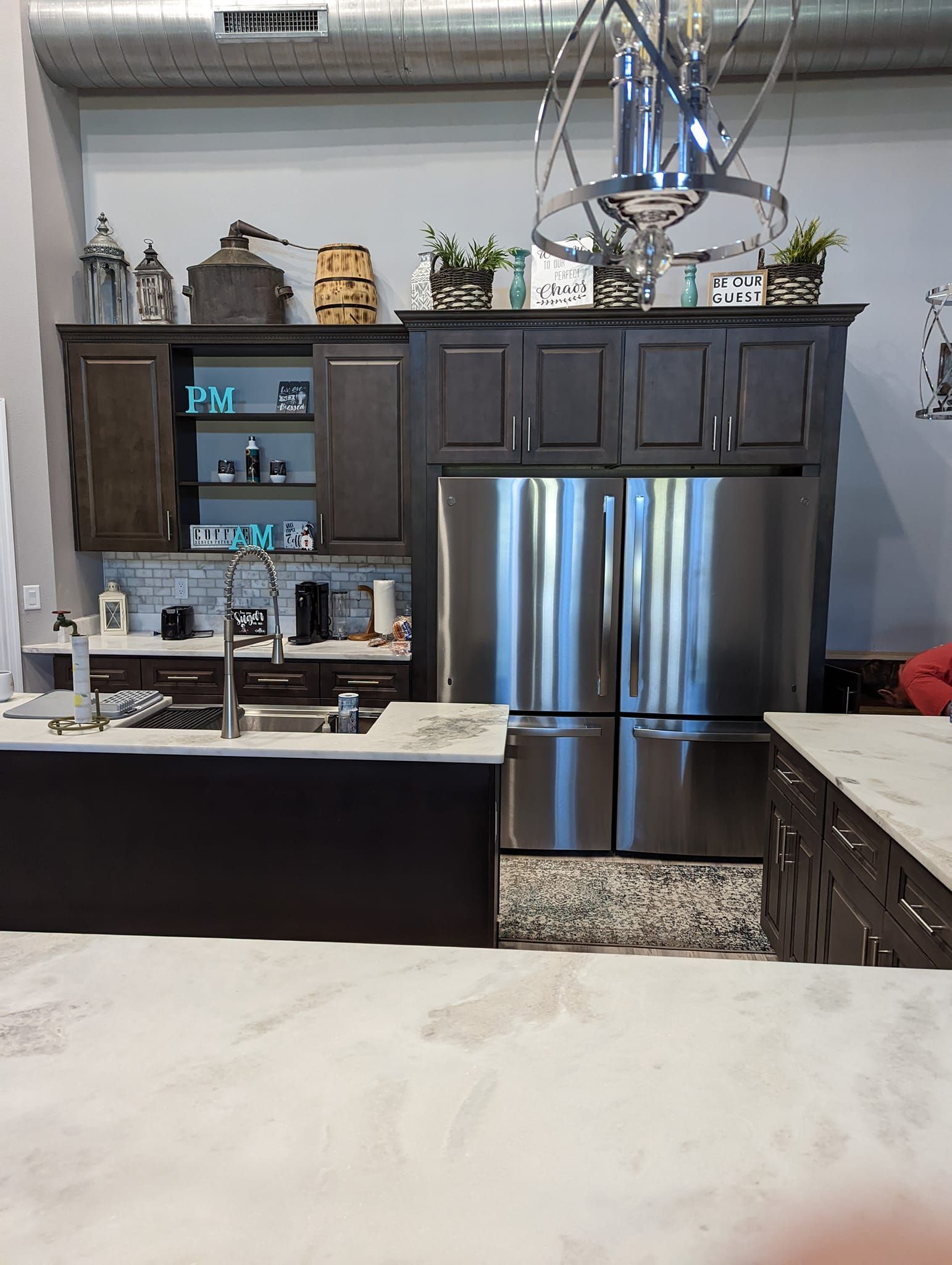 Kitchen with dark cabinets, stainless steel refrigerator, and island with a sink.