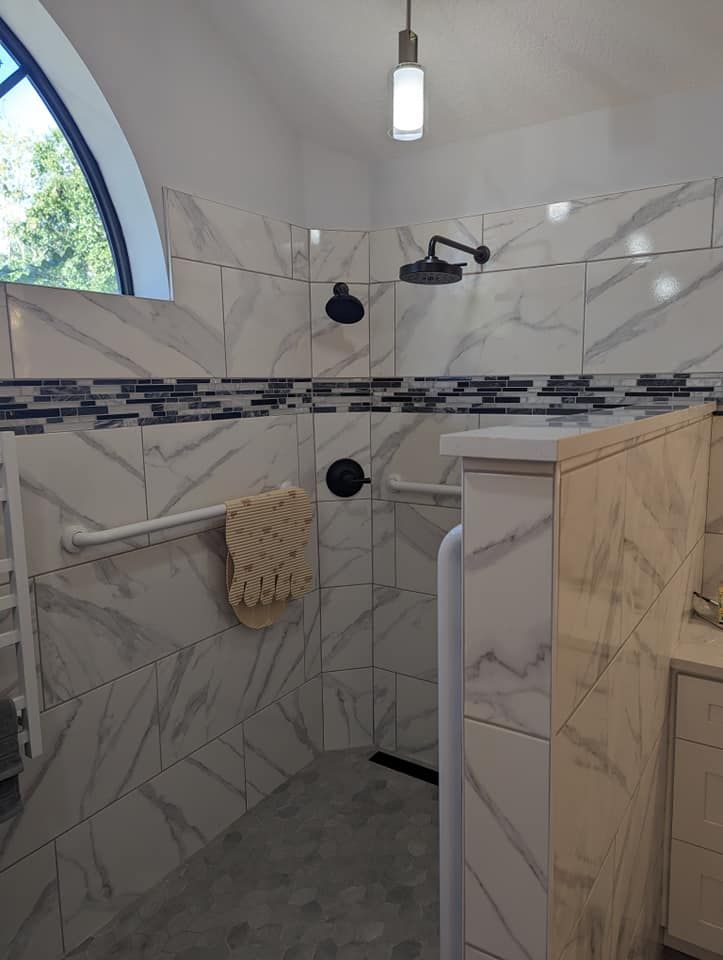 Modern shower with marble-look tiles, black fixtures, and a glass accent. Includes grab bar and built-in bench.