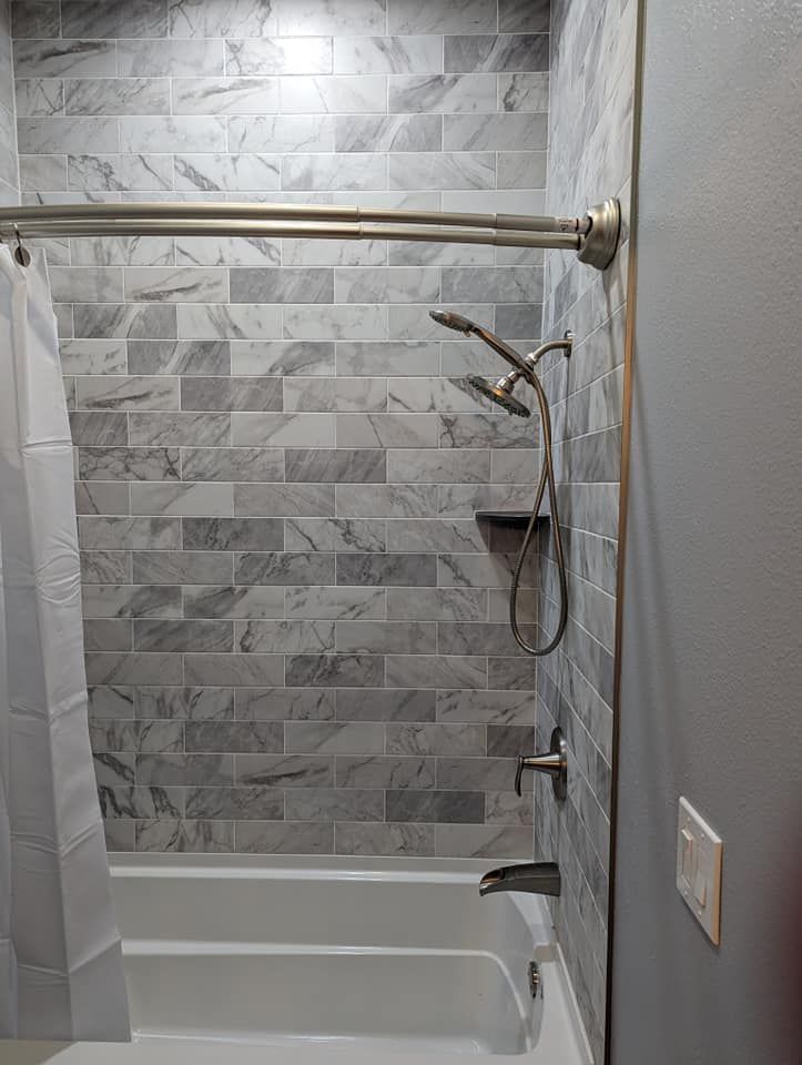 Bathroom with grey marble-look tiled shower walls and a white bathtub, showerhead, and curtain.