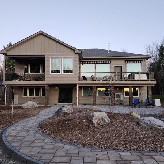 Two-story beige house with stone columns and a paved walkway leading to the entrance.