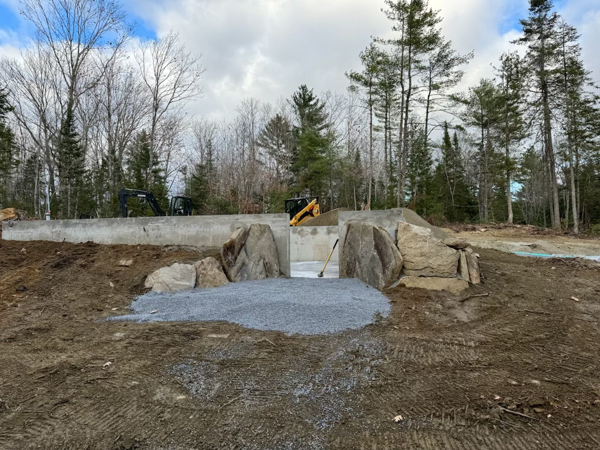 A concrete structure is being built in the middle of a dirt field surrounded by trees.
