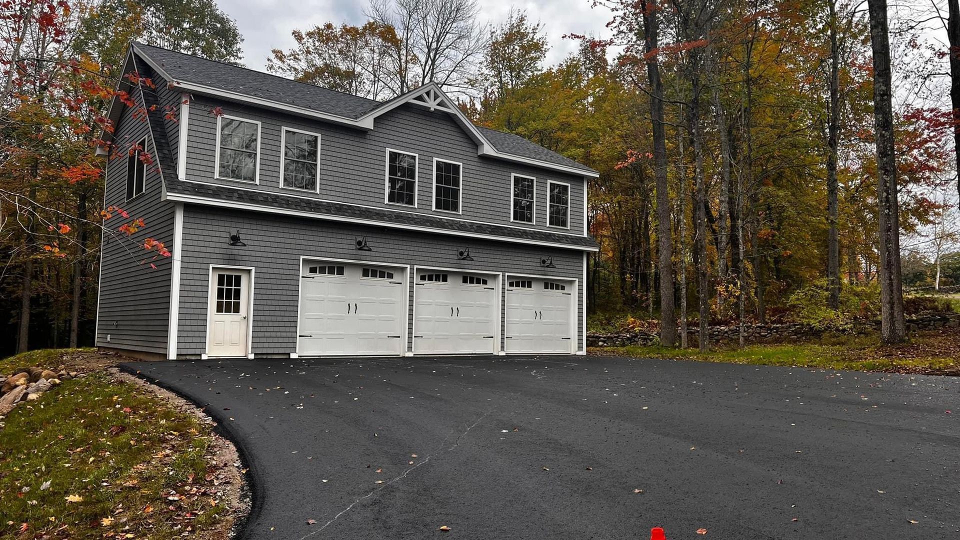 A large house with three garage doors is surrounded by trees.