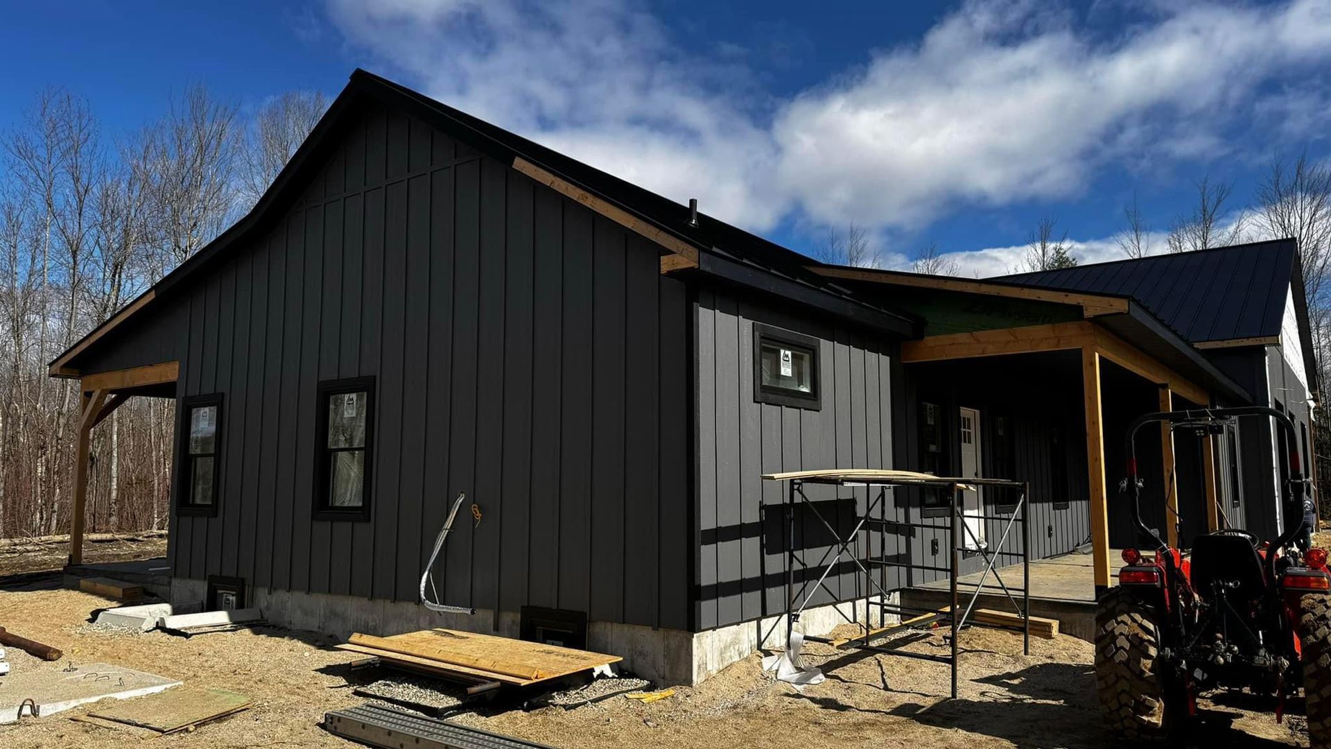 A black house is being built with a tractor parked in front of it.