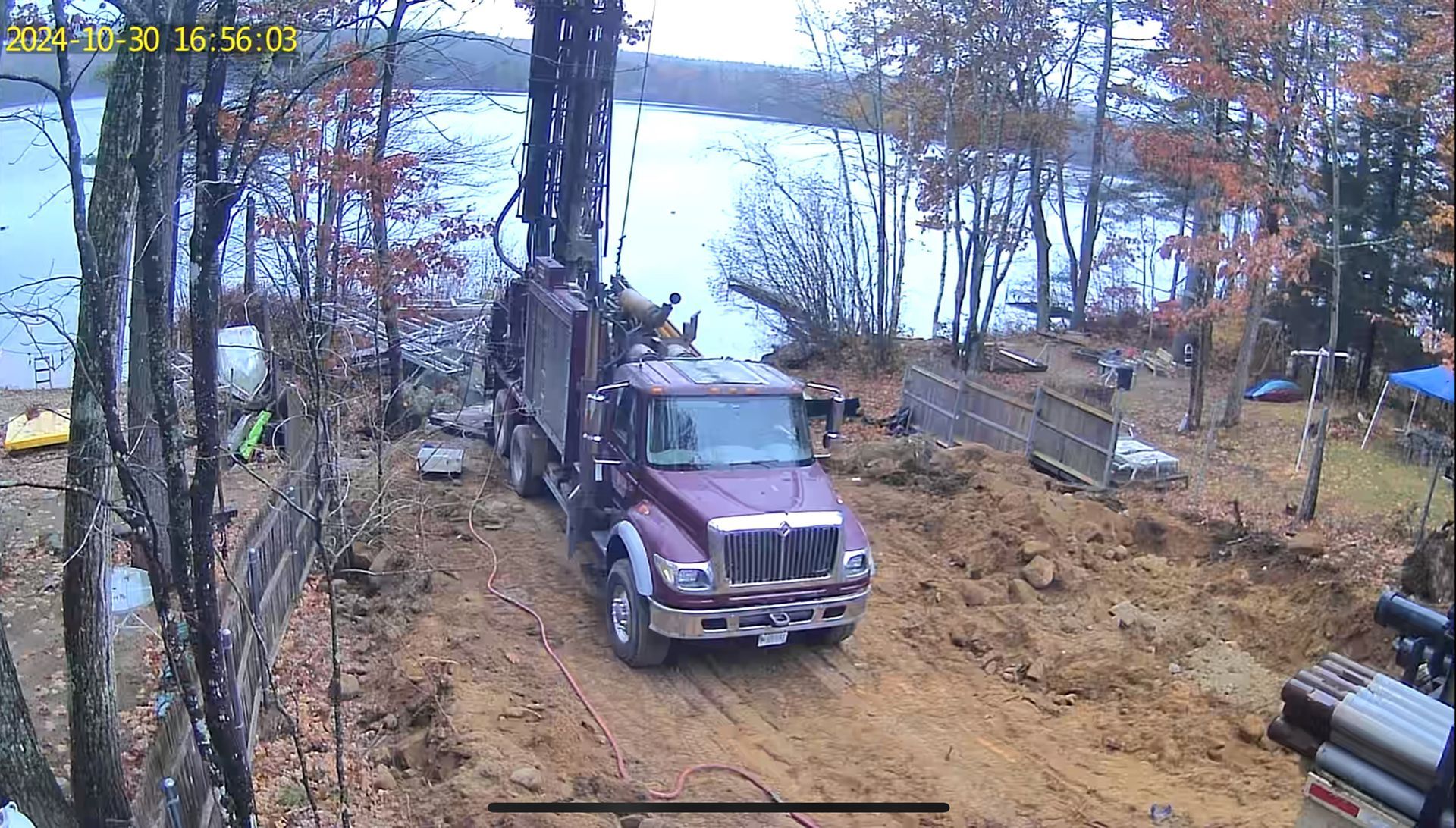 A red truck is driving down a dirt road next to a body of water.