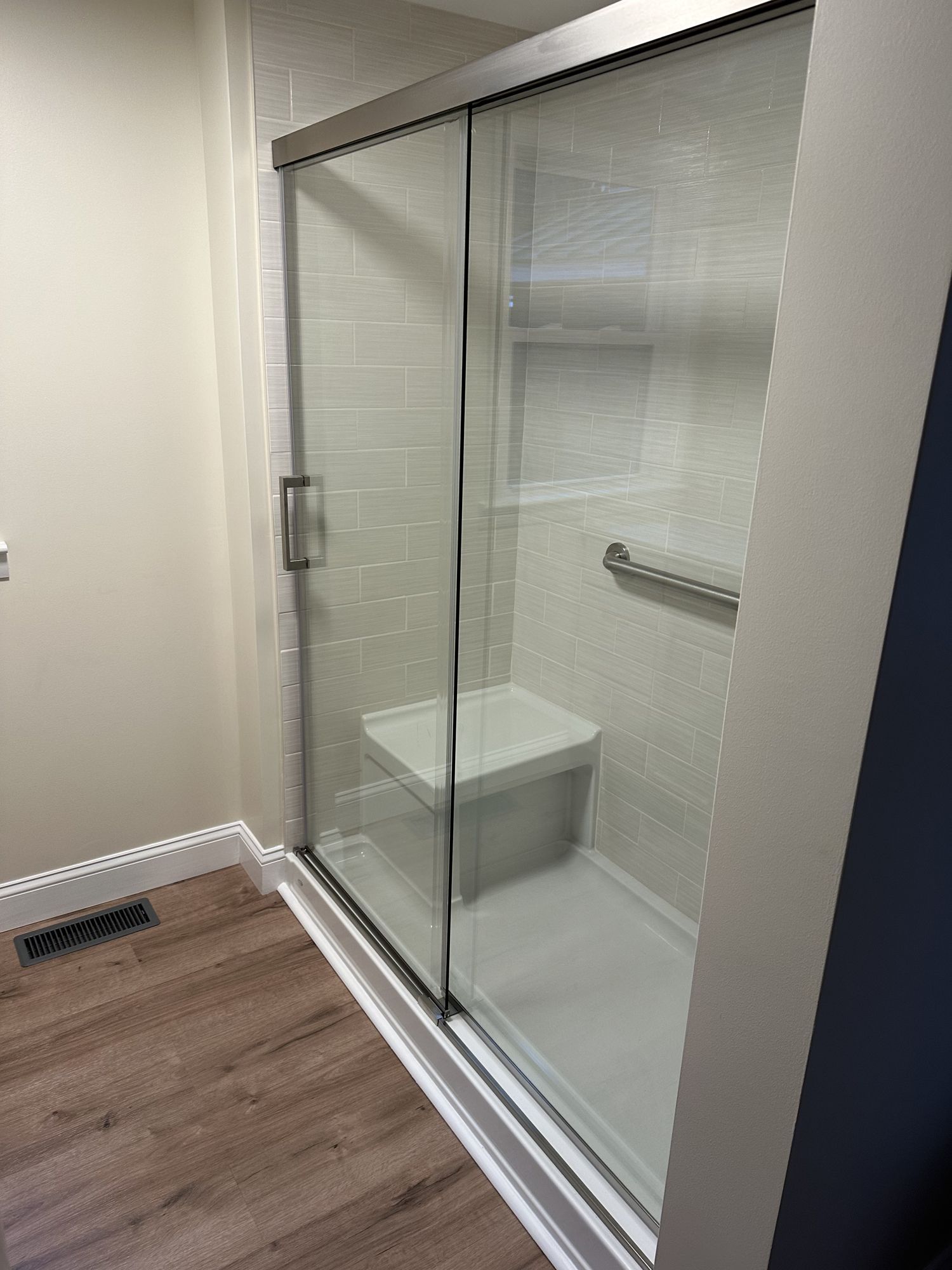A bathroom with a sliding glass shower door and a bench.