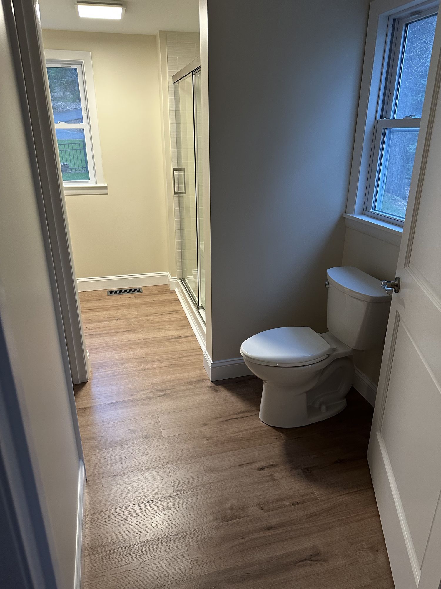 A bathroom with a toilet , shower and window.