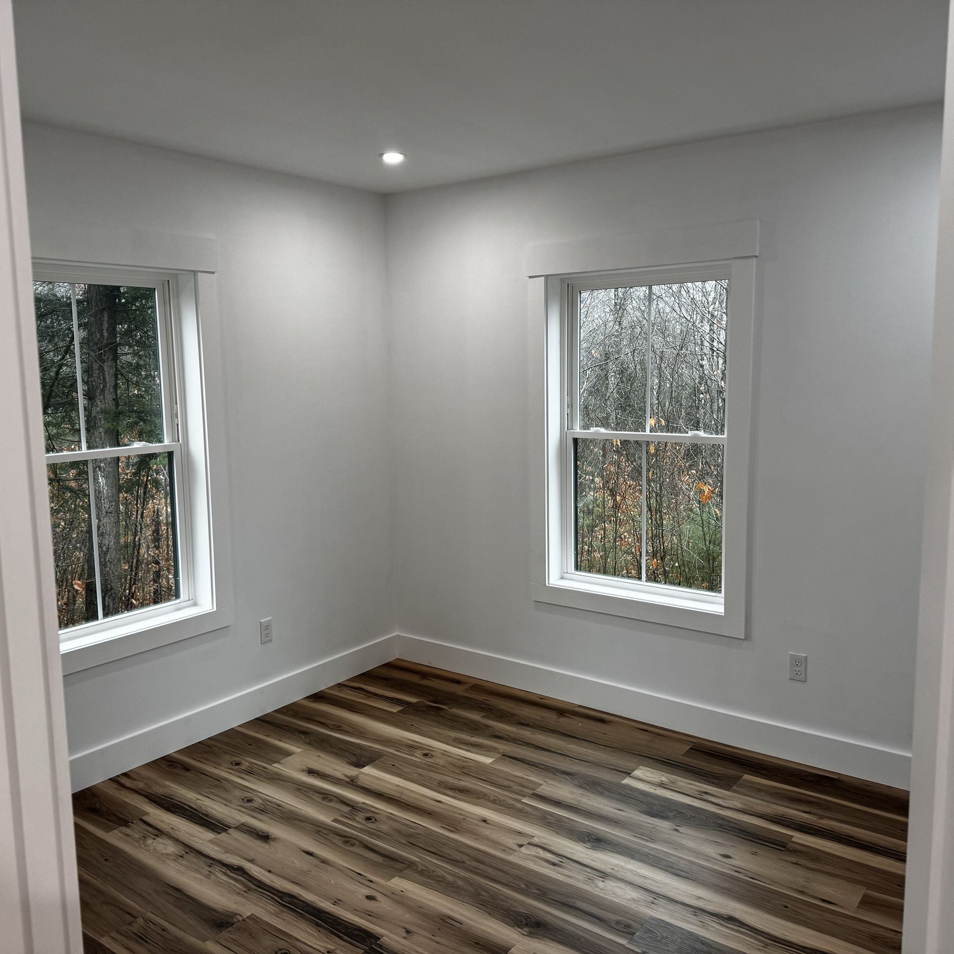 An empty room with hardwood floors and two windows