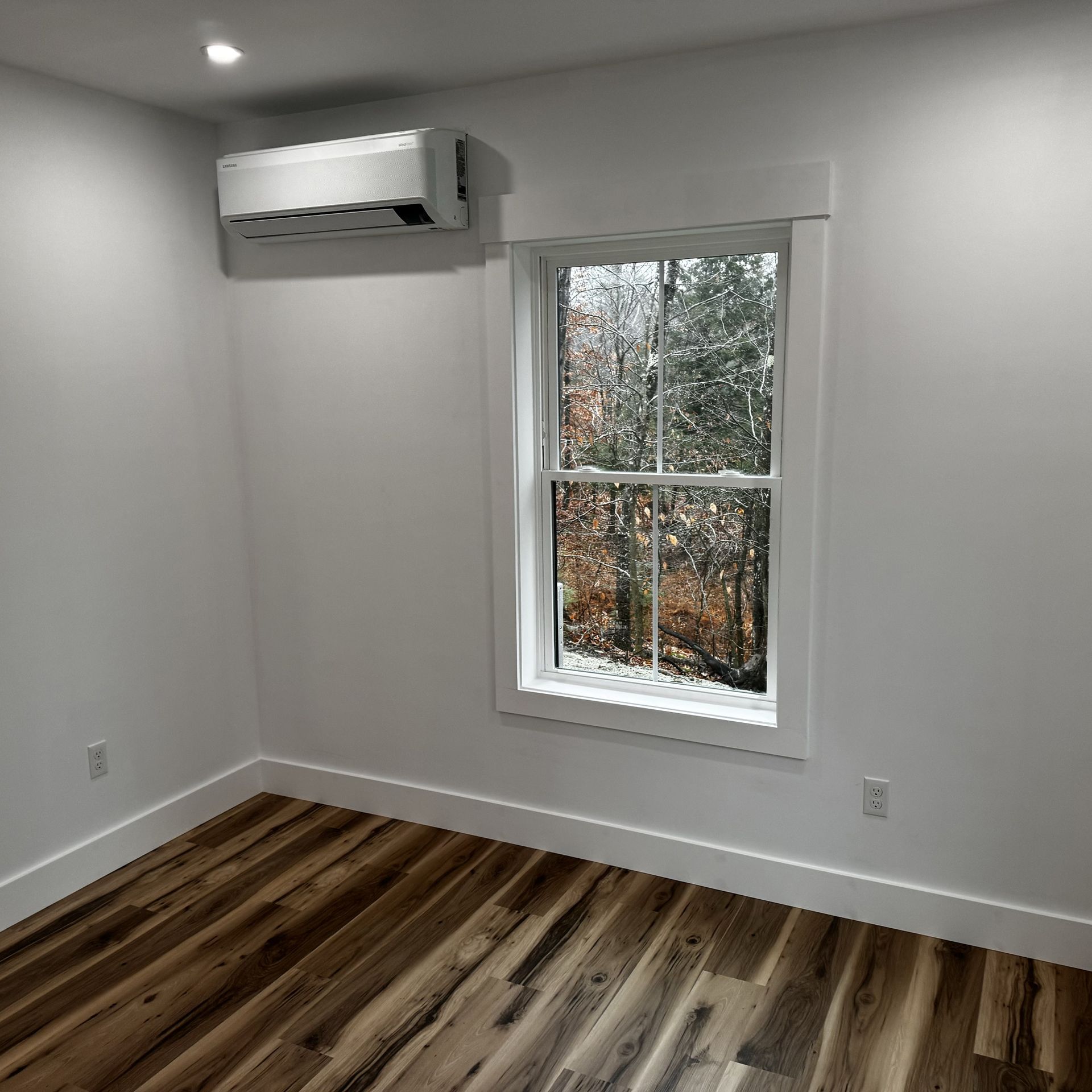 An empty room with hardwood floors and a window.
