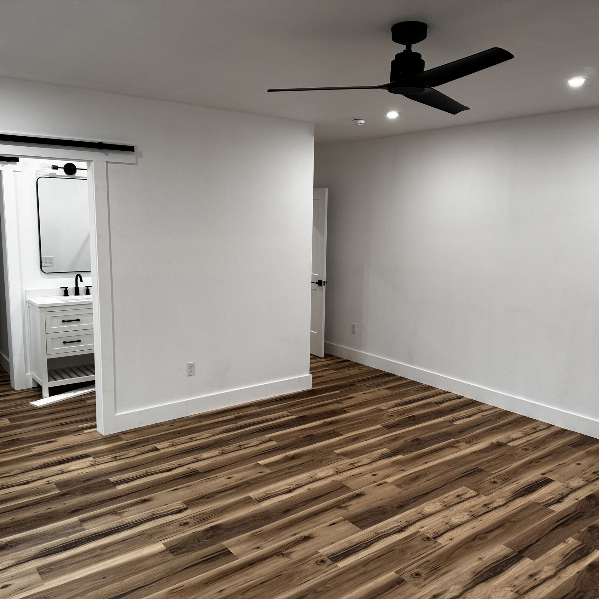 An empty room with a wooden floor and a ceiling fan.