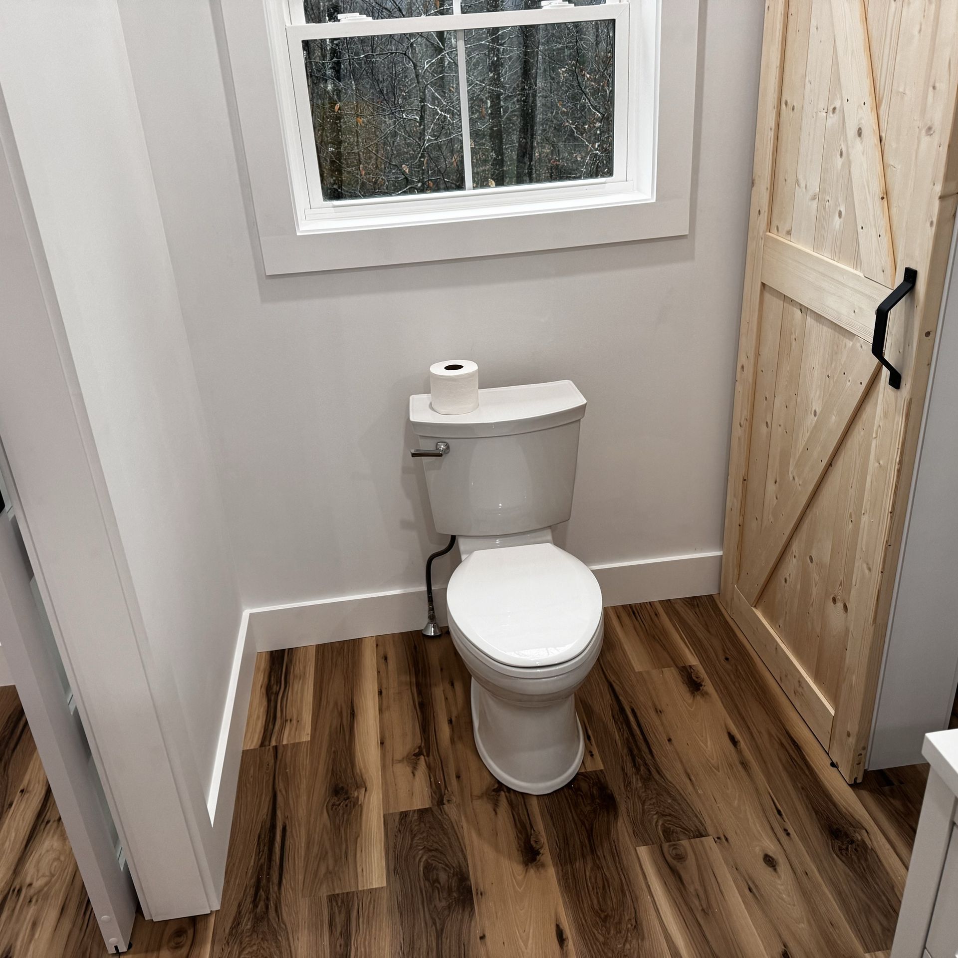 A toilet is sitting in a bathroom next to a window and a wooden door.