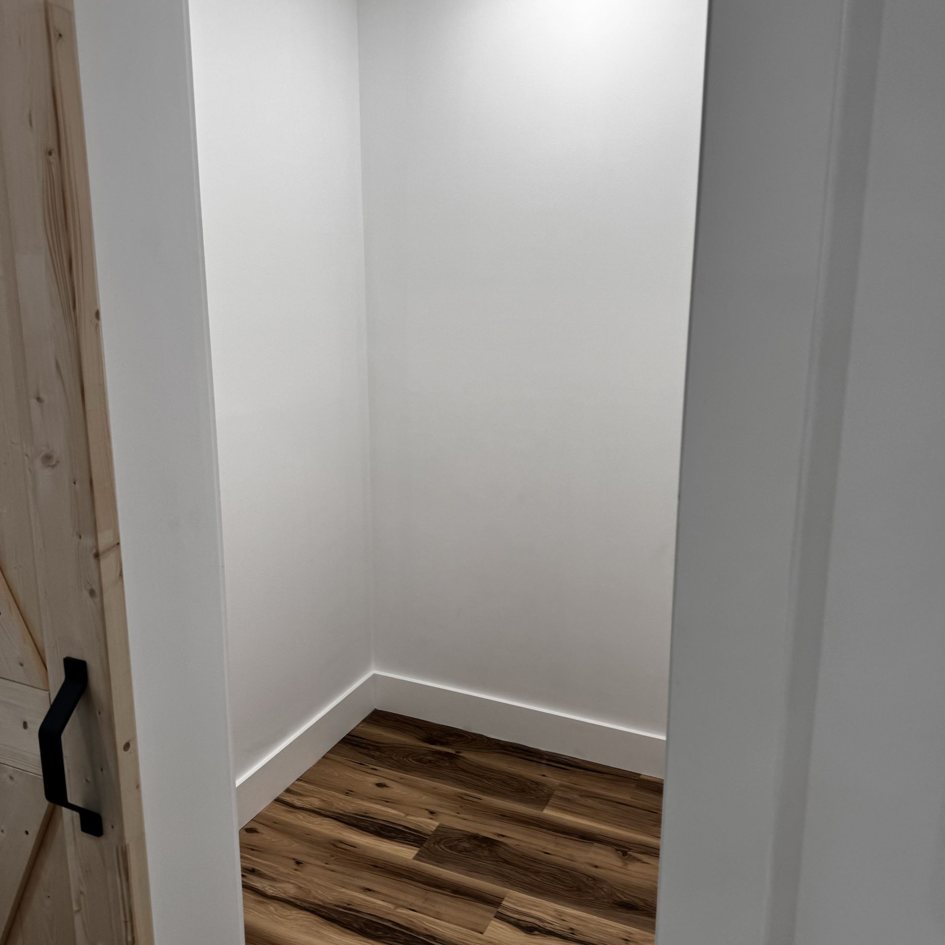 An empty closet with a wooden floor and white walls.