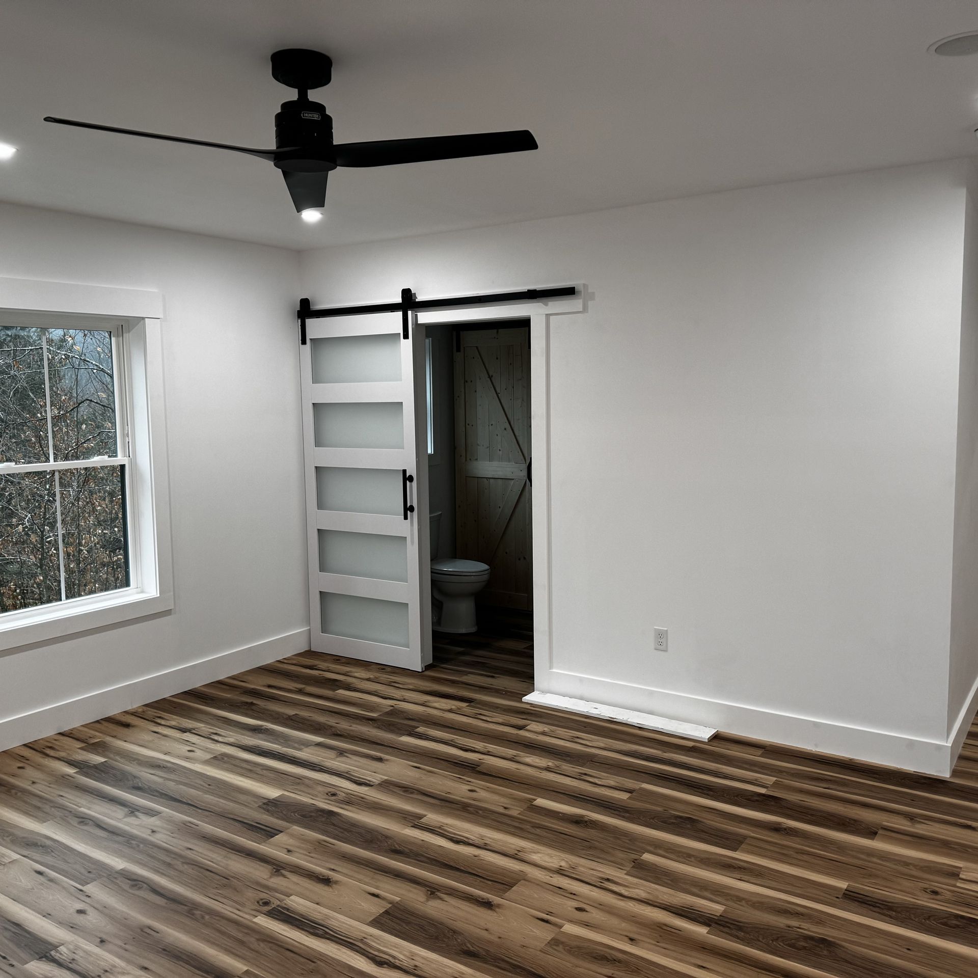 An empty room with a ceiling fan and a sliding barn door leading to a bathroom.