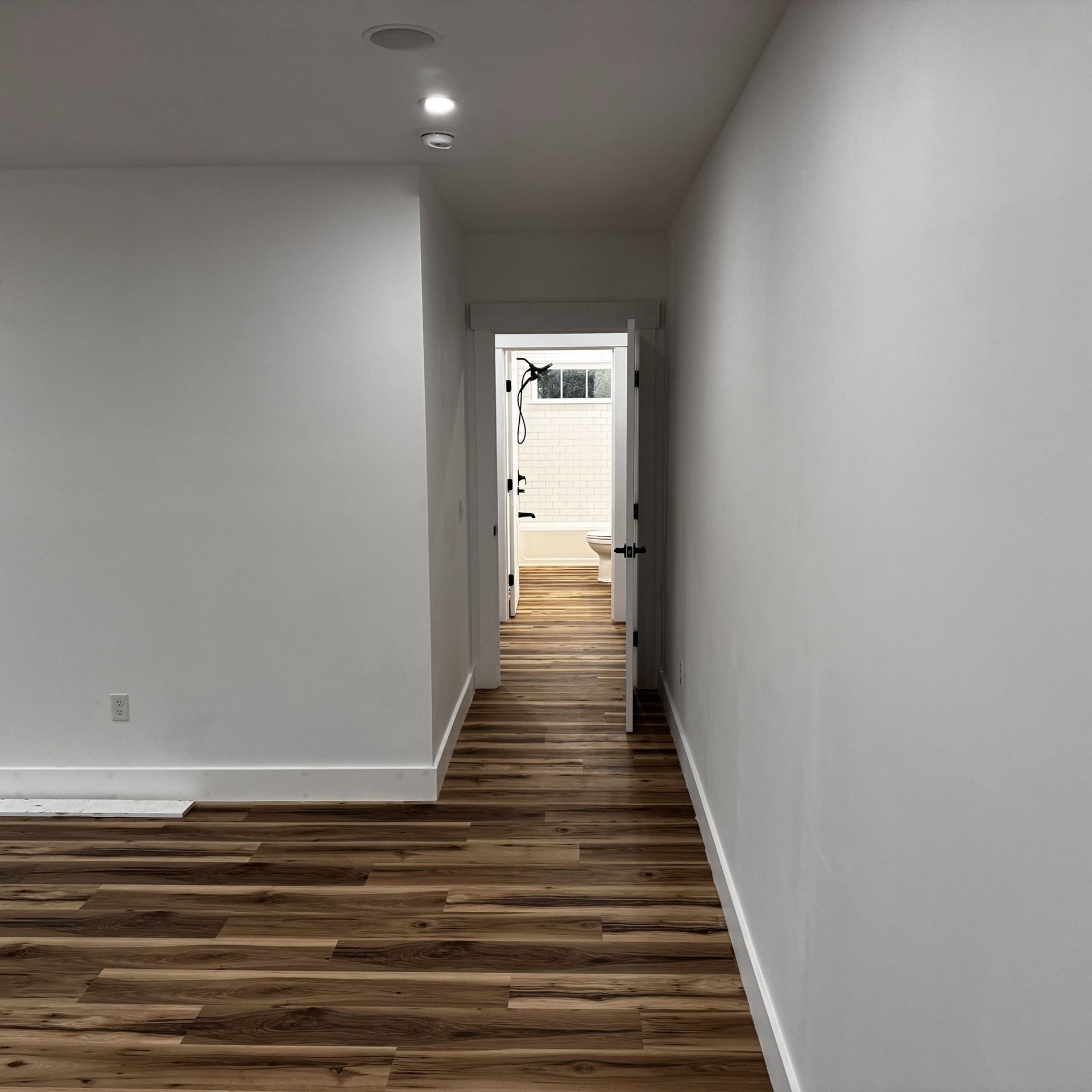 A hallway with wooden floors and white walls leading to a bathroom.