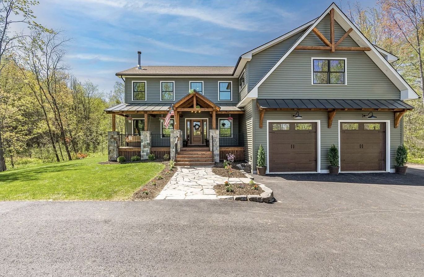 A large house with two garages is sitting on top of a lush green field.