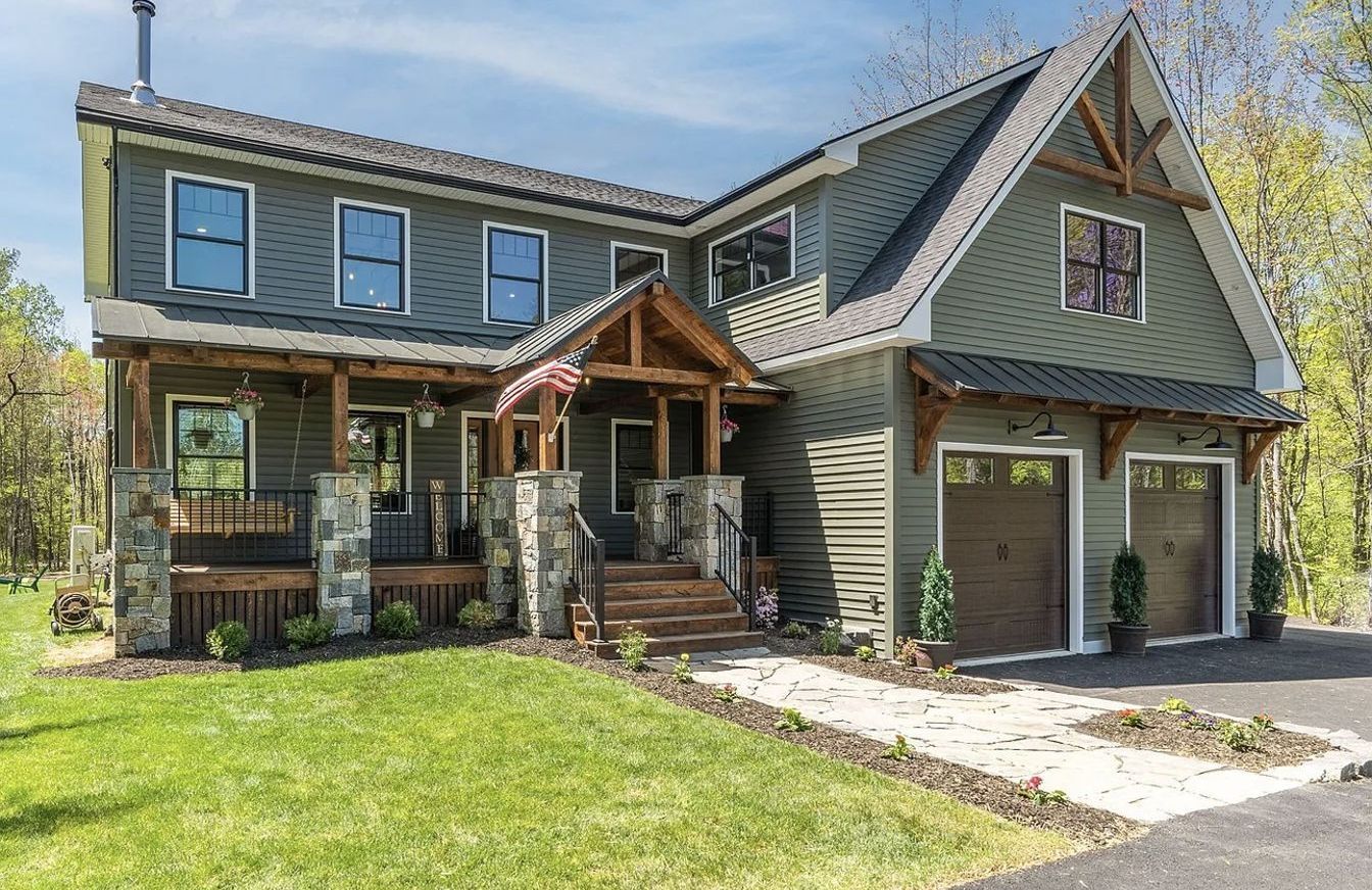 A large house with two garages and a porch is sitting on top of a lush green field.